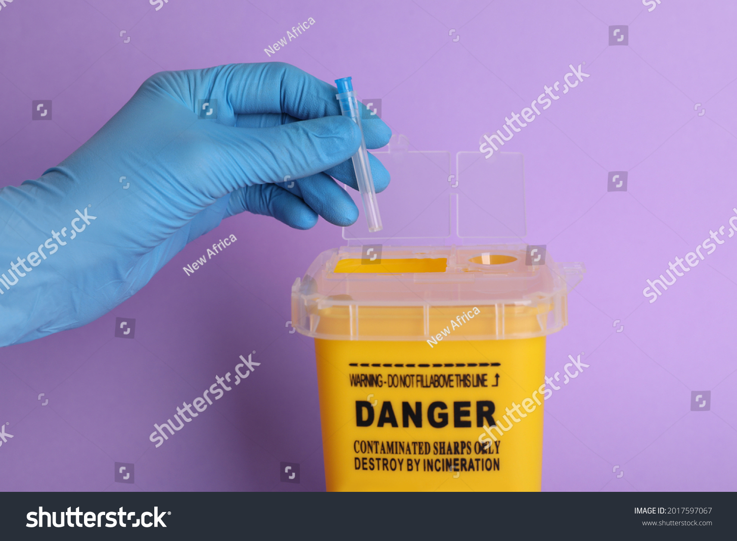 Doctor throwing used syringe needle into sharps container on violet background, closeup #2017597067