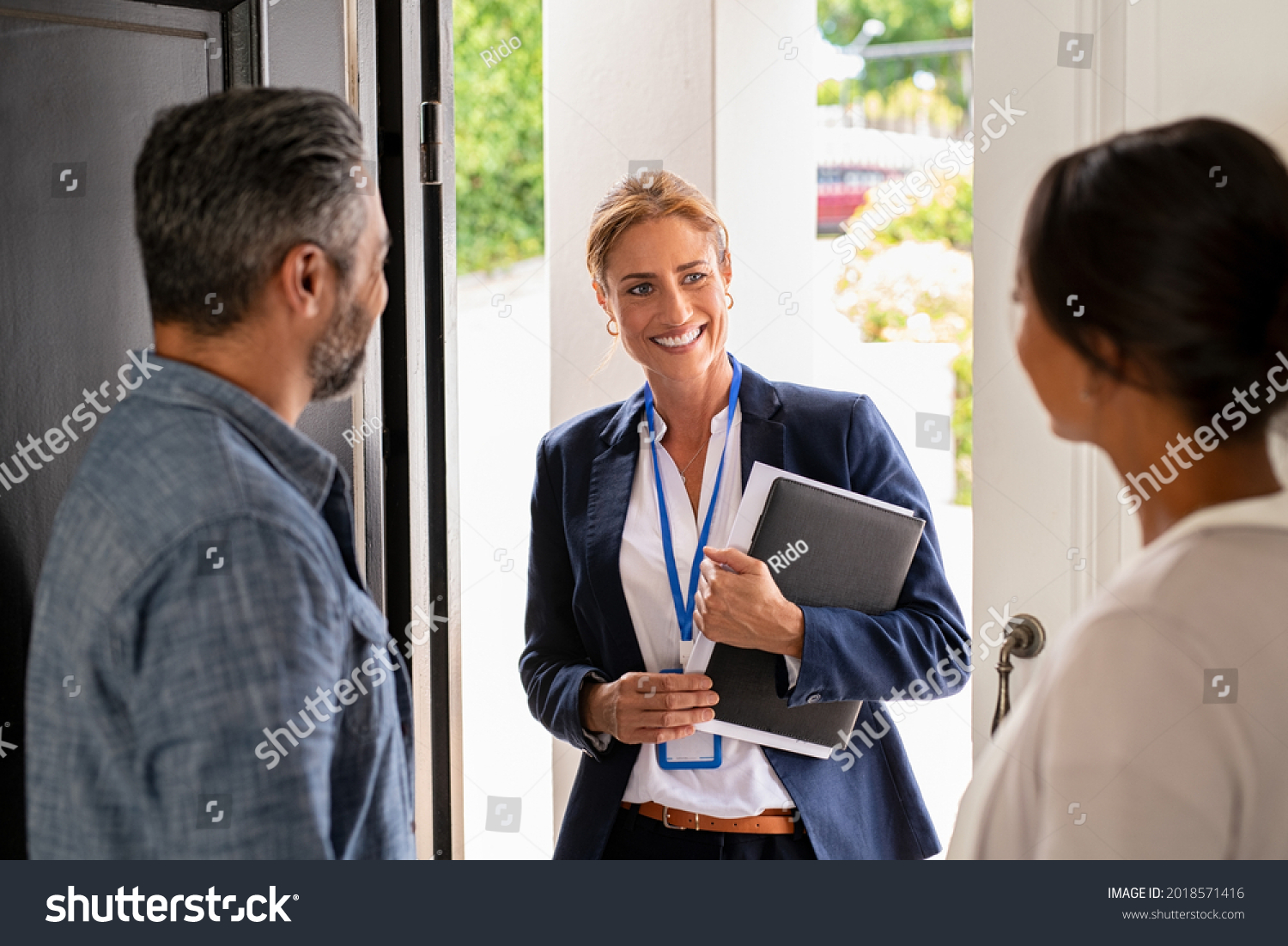 Smiling mature social counselor meeting mature couple at home. Happy multiethnic man and latin woman greeting agent at home standing near door. Successful social worker consultant on the doorstep. #2018571416