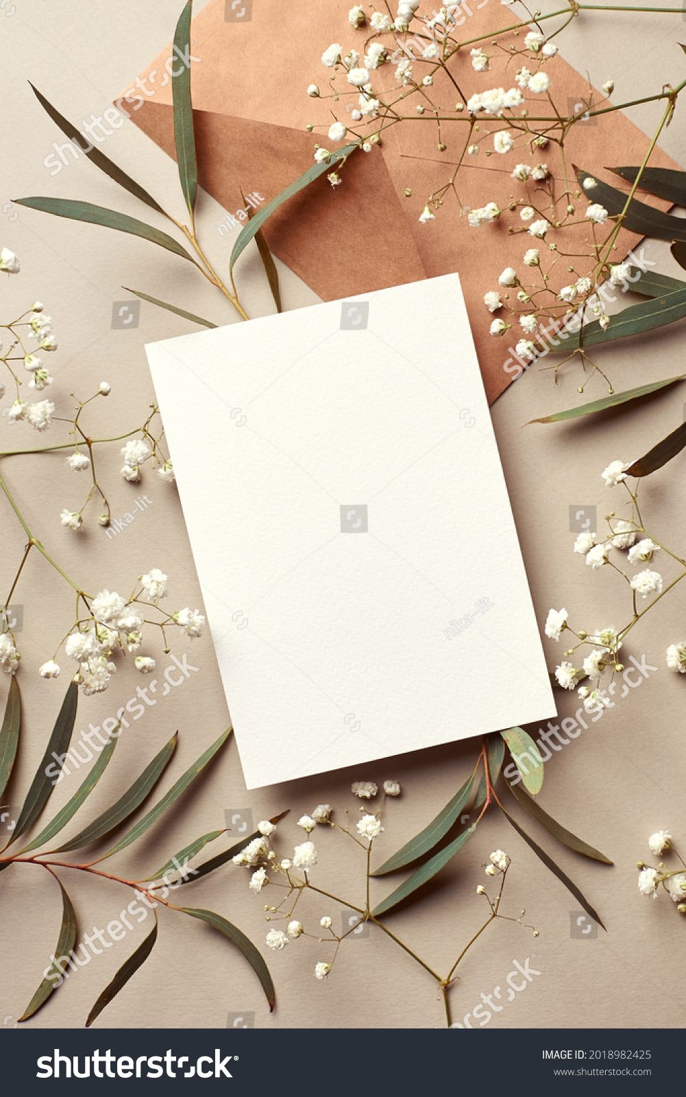 Invitation or greeting card mockup with craft paper envelope, eucalyptus and gypsophila twigs. Card mockup with copy space on beige background. #2018982425