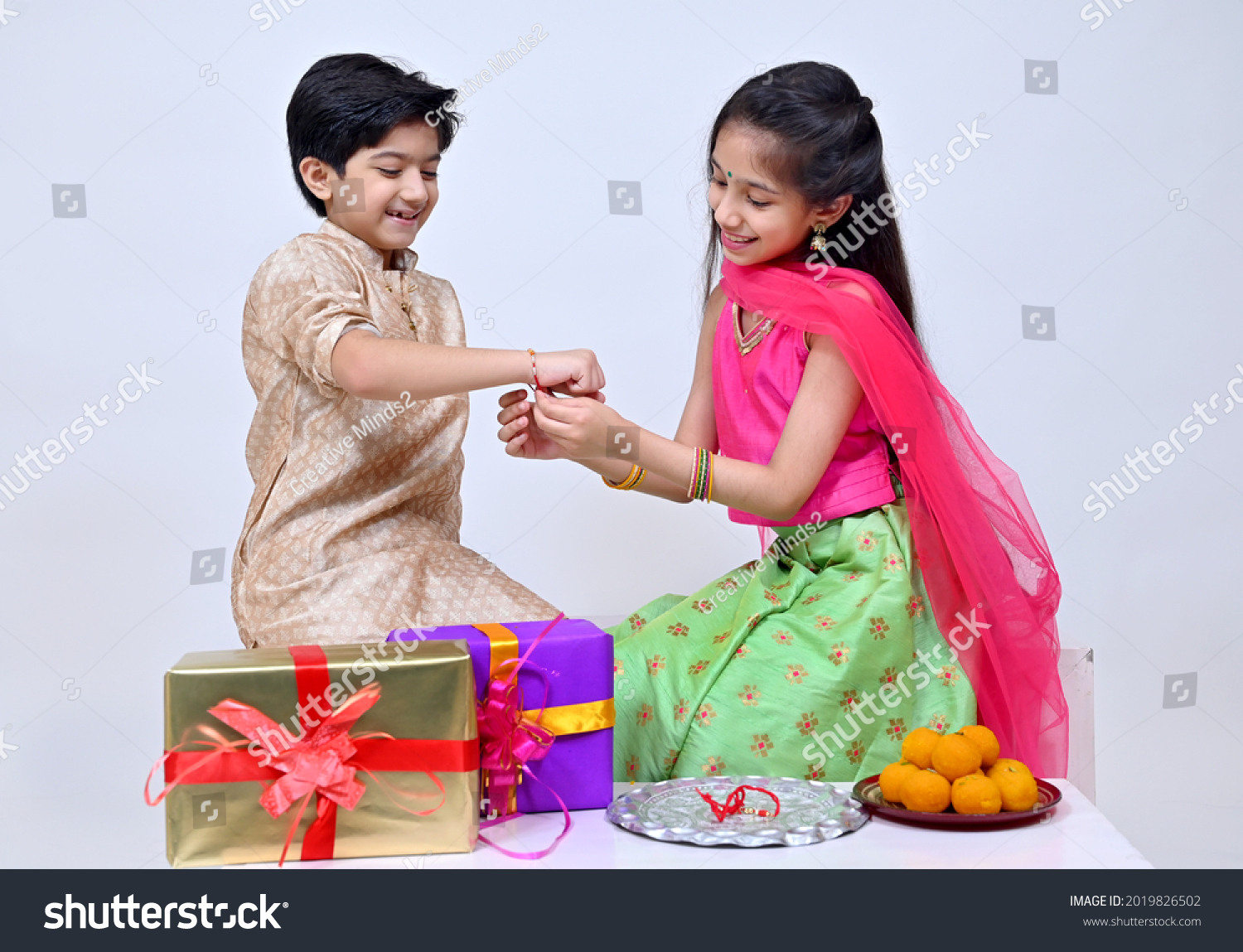Hindu Brother and sister  in ethnic wear holding Indian sweets and gift box on the occasion of Raksha Bandhan festival #2019826502