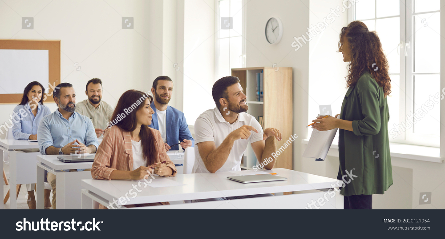 College teacher or business course trainer having discussion with group of people. Happy adult students sitting at tables in classroom, having training class and learning new things. Education concept #2020121954