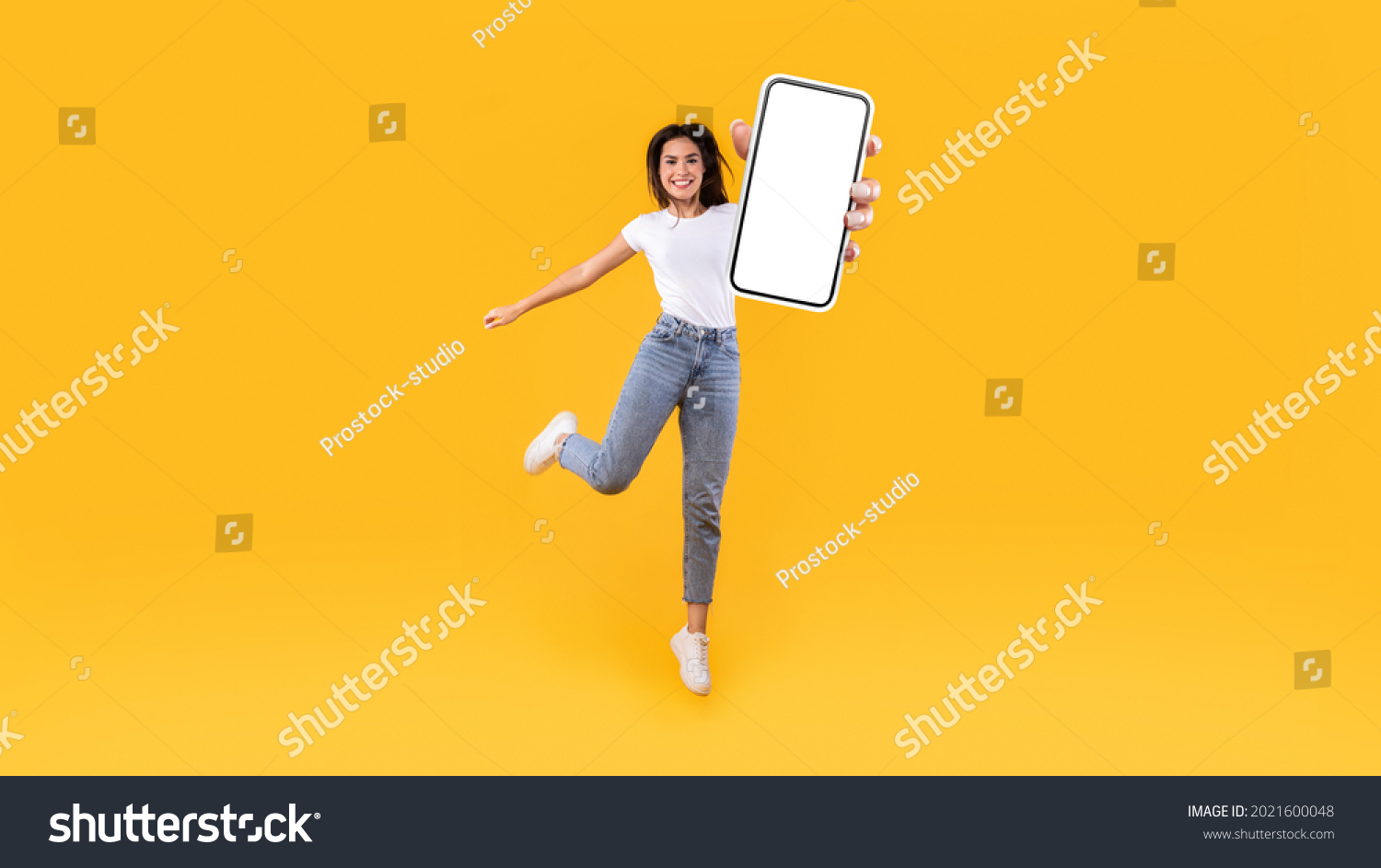 Happy young woman showing empty cellphone screen while jumping up on yellow studio background, collage, full body length, banner panorama. Excited lady recommending nice and useful mobile application #2021600048