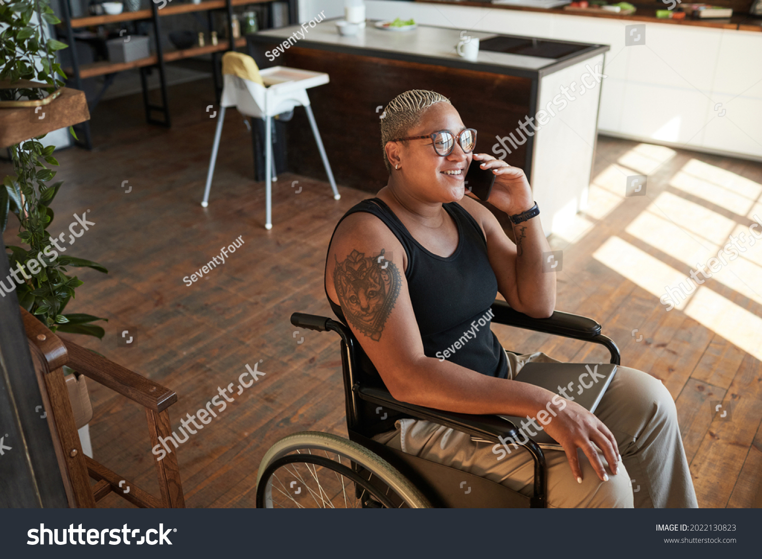 High angle portrait of contemporary tattooed woman with disability speaking by smartphone while working from home, copy space #2022130823