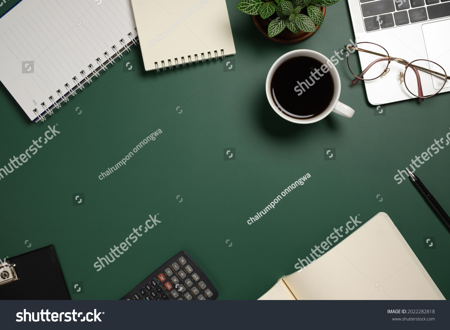 Desk office with laptop, blank notebook, flower, coffee cup, glasses and pen on green table. Flat lay top view copy space. Home office. #2022282818