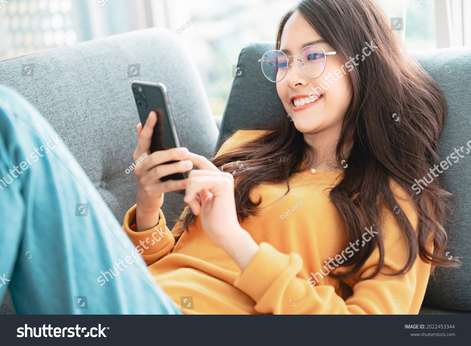 Happy asian woman using mobile phone. Smiling young female using app shopping online, ordering delivery relax on sofa at home. #2022453344