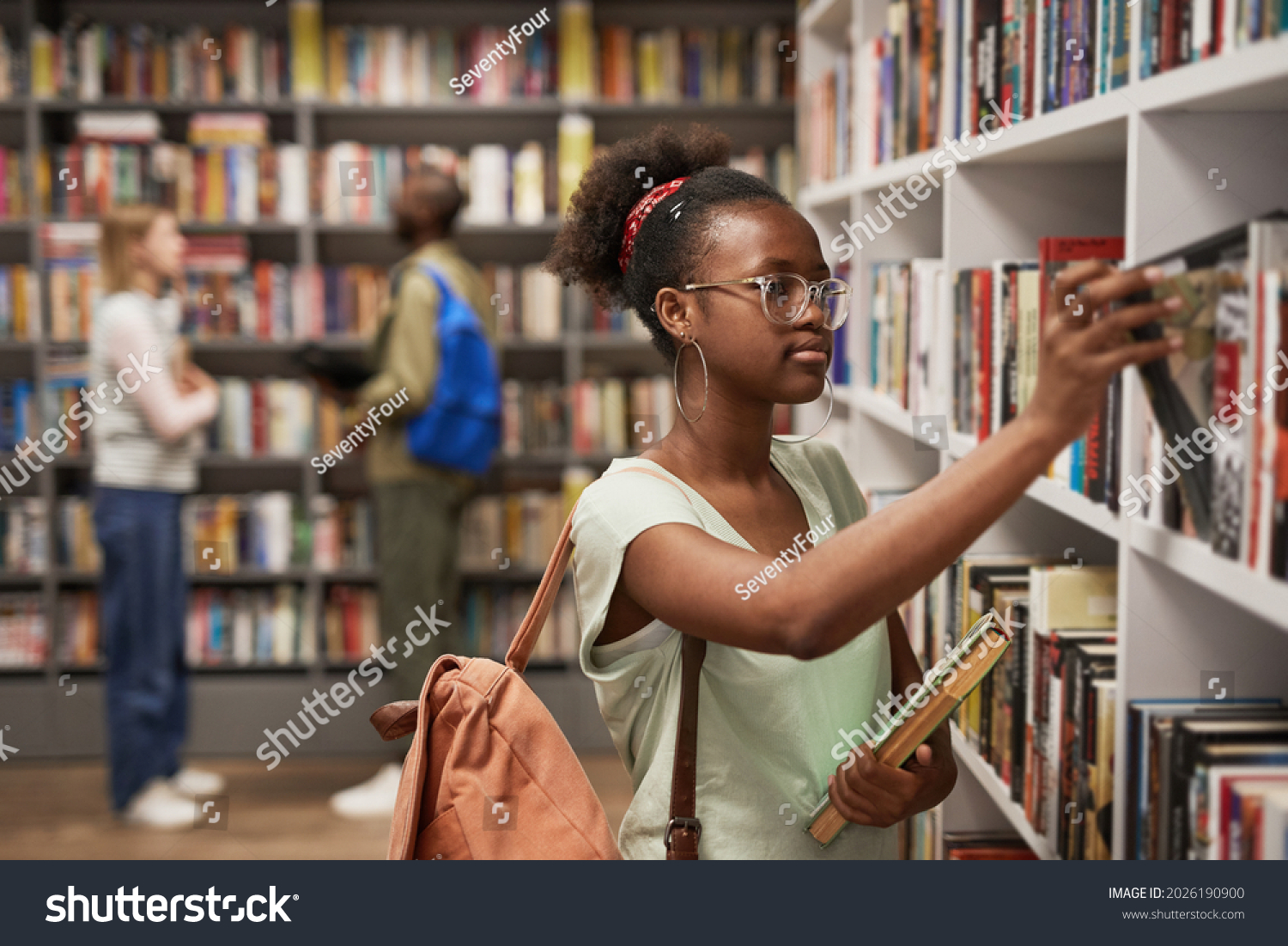 Waist up portrait of female Africa-American student choosing books in college library, copy space #2026190900