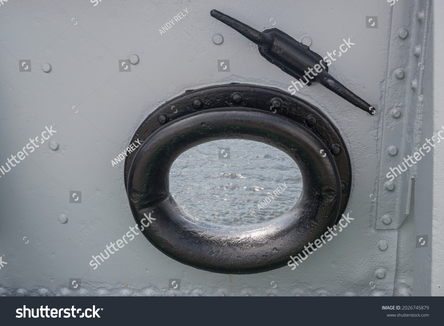 Mooring fairlead with round hole and black cast-iron ring with smooth rounding on ship is installed in gray riveted bulwark. Above is casted horn nearby. Sea water is visible in opening of fairlead. #2026745879