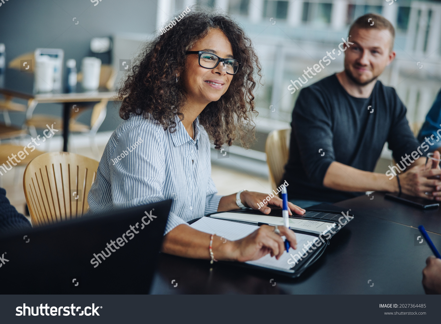 Mature businesswoman with a file sitting in meeting with her team. Female entrepreneur having meeting with colleagues in boardroom. #2027364485