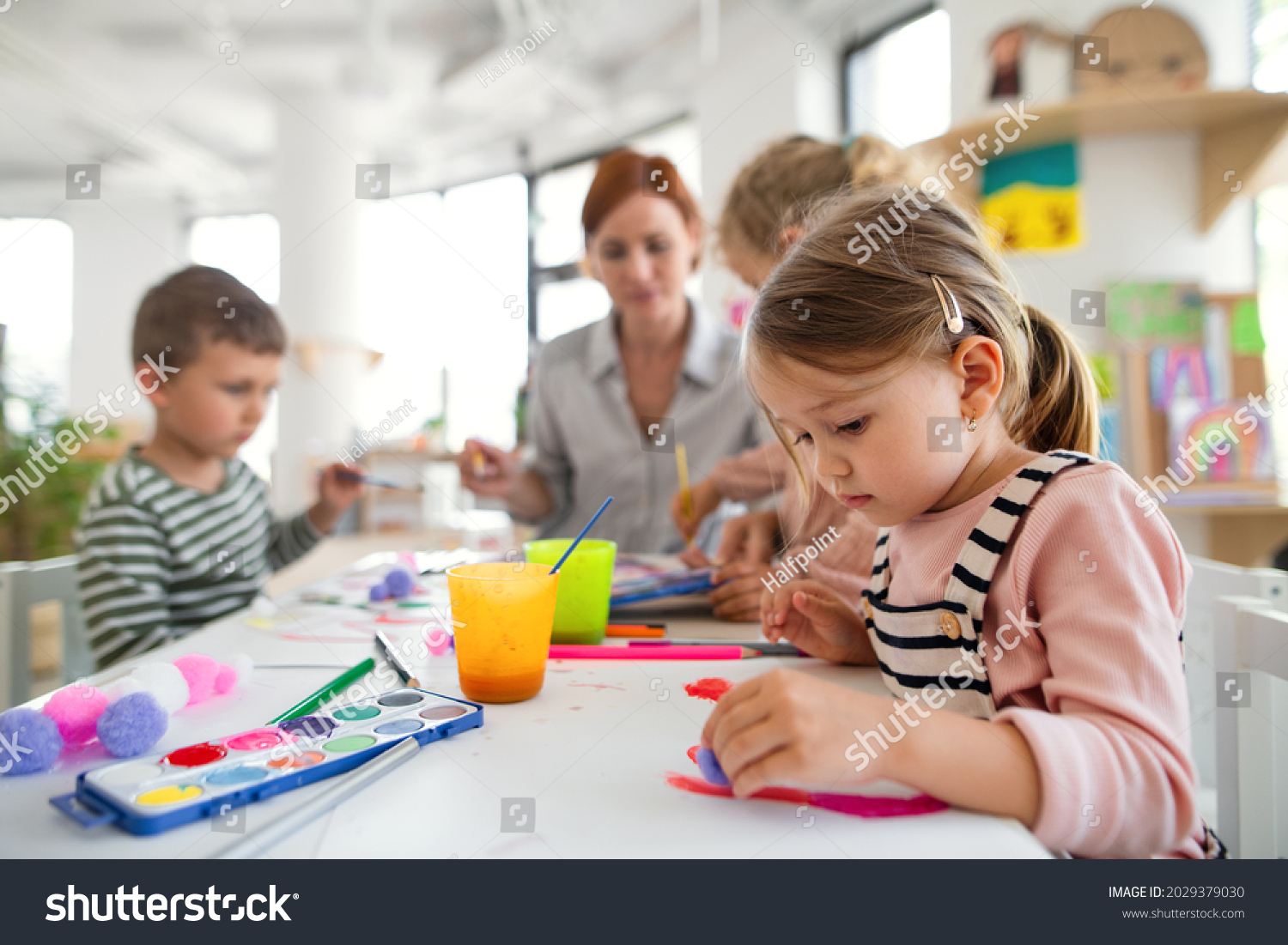 Group of small nursery school children with teacher indoors in classroom, painting. #2029379030