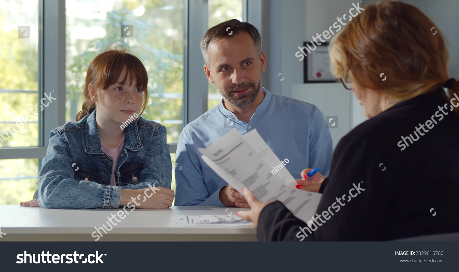 Back view of female headmaster interview father and preteen girl in school office. Smiling mature man with teenage daughter meeting woman principal #2029615760