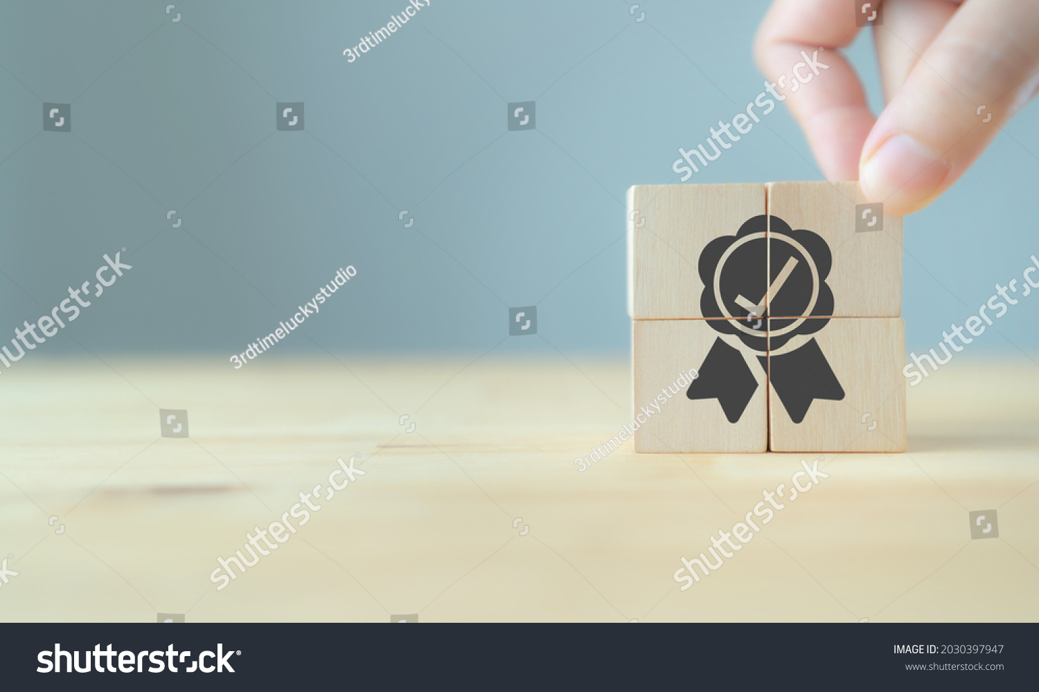 Quality warranty concept. Man's hand puts the wooden cubes with quality warranty icon on wooden cubes with grey background. Used for banner and advertising product and service quality commitment. #2030397947