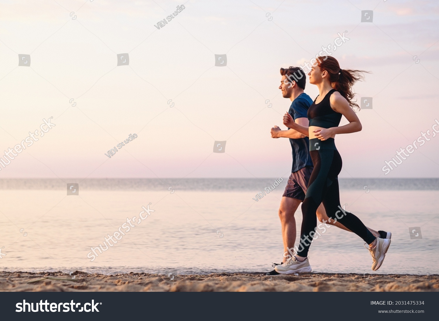 Full body profile couple young two friends strong sporty sportswoman sportsman woman man 20s in sport clothes warm up training run on sand sea ocean beach outdoor jog on seaside in summer day morning #2031475334