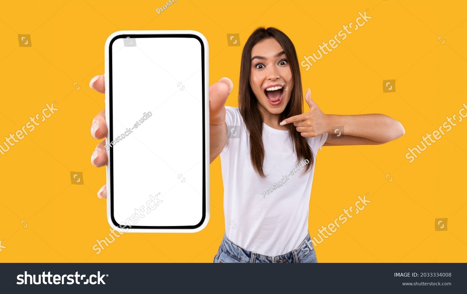 Great Mobile Offer. Excited Lady Pointing Finger At Smartphone In Her Hand, Emotionally Reacting To New App, Overjoyed Millennial Woman Standing Isolated Over Orange Studio Background, Panorama #2033334008