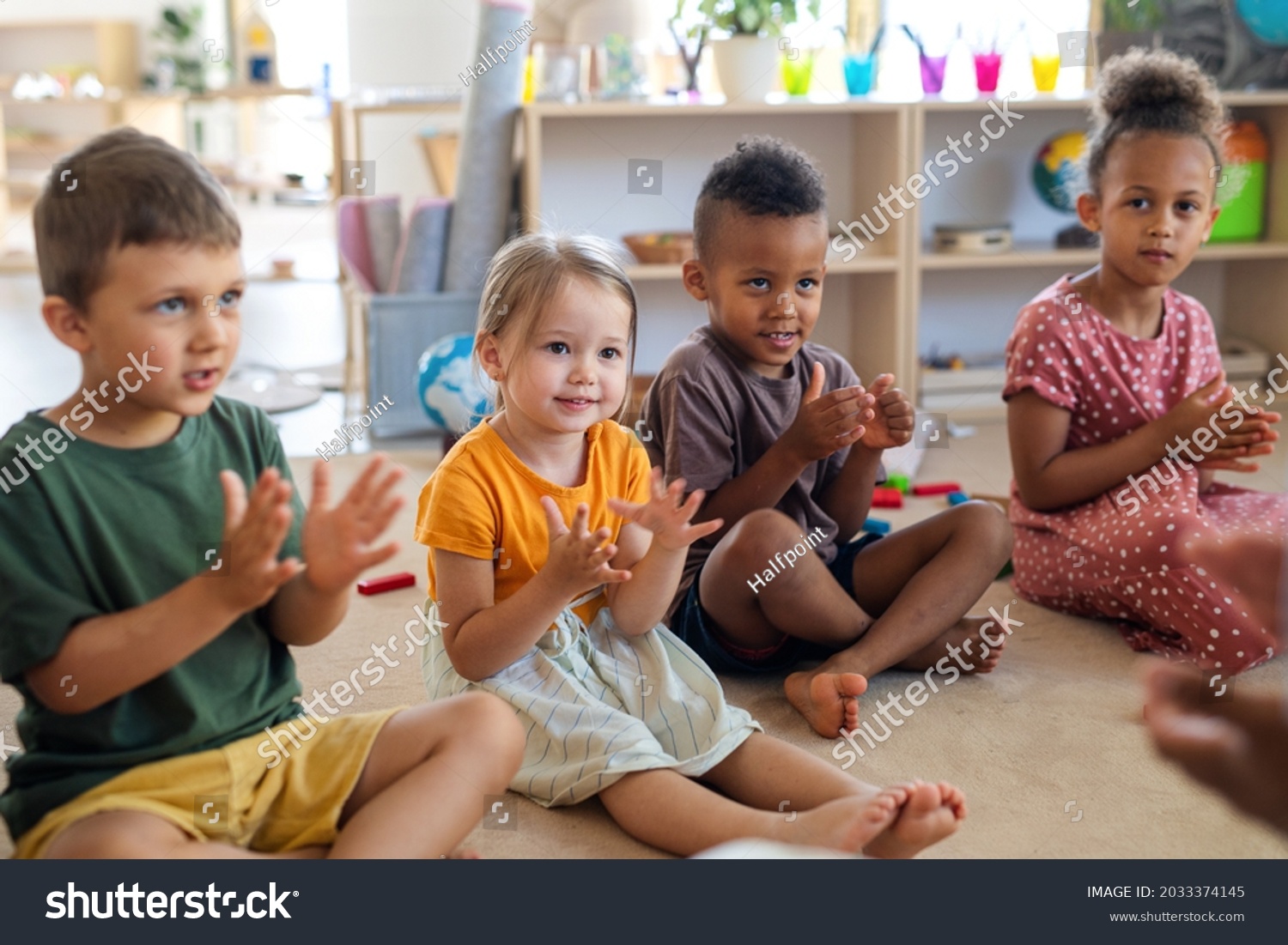 Group of small nursery school children sitting on floor indoors in classroom, clapping. #2033374145
