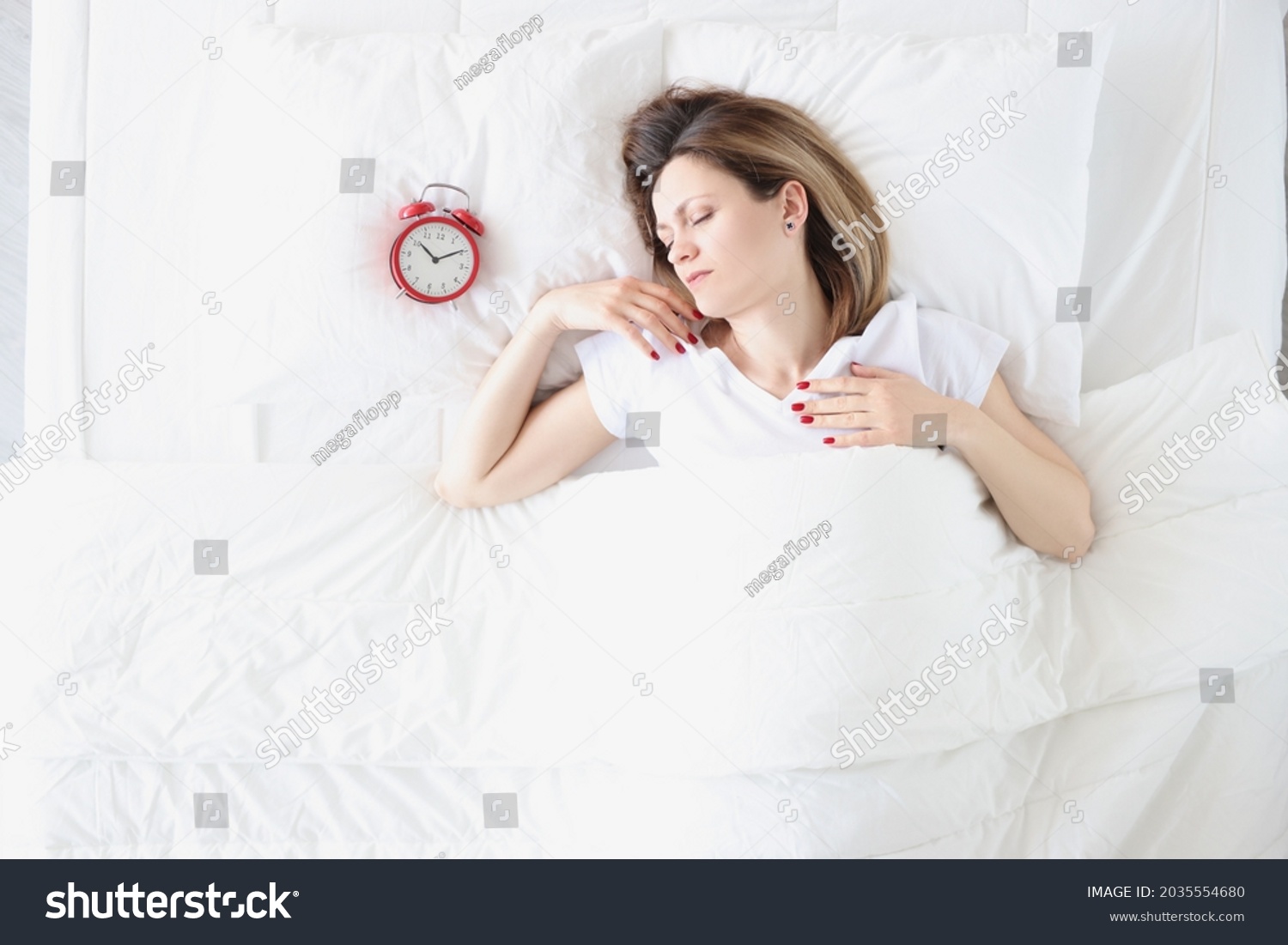 Young woman lying in bed near red alarm clock top view #2035554680