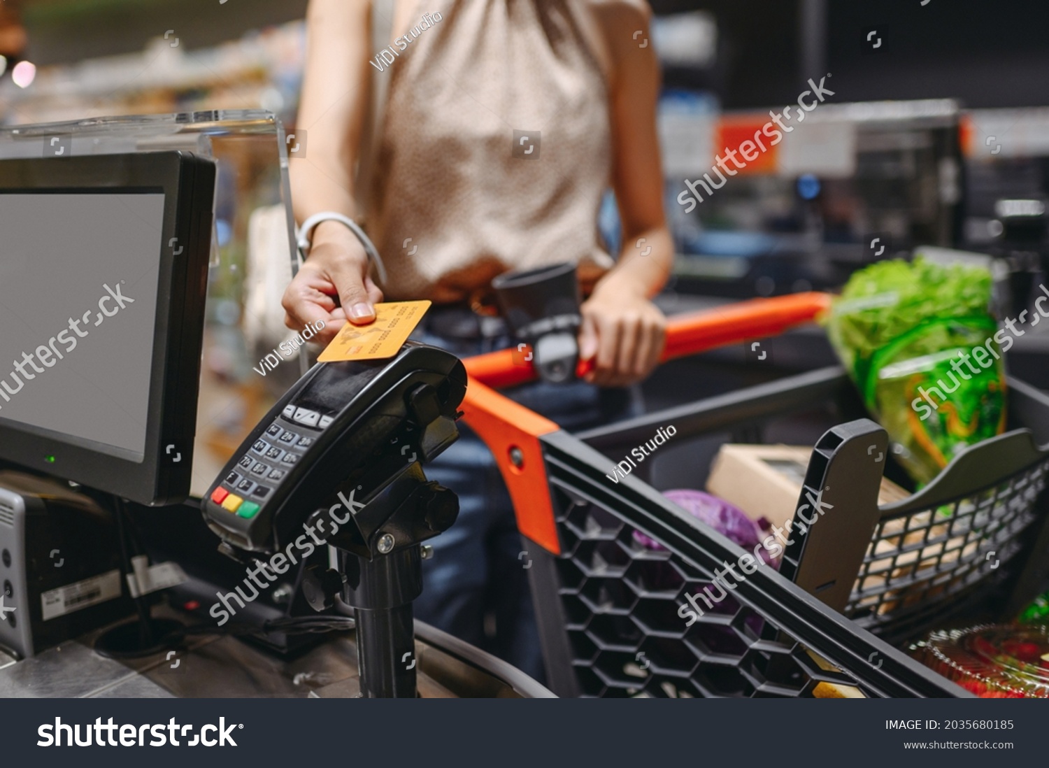 Cropped close up woman hand shopping at supermaket put credit card to wireless modern bank payment terminal process acquire payments near cashier checkout with cart inside store. Purchasing concept #2035680185