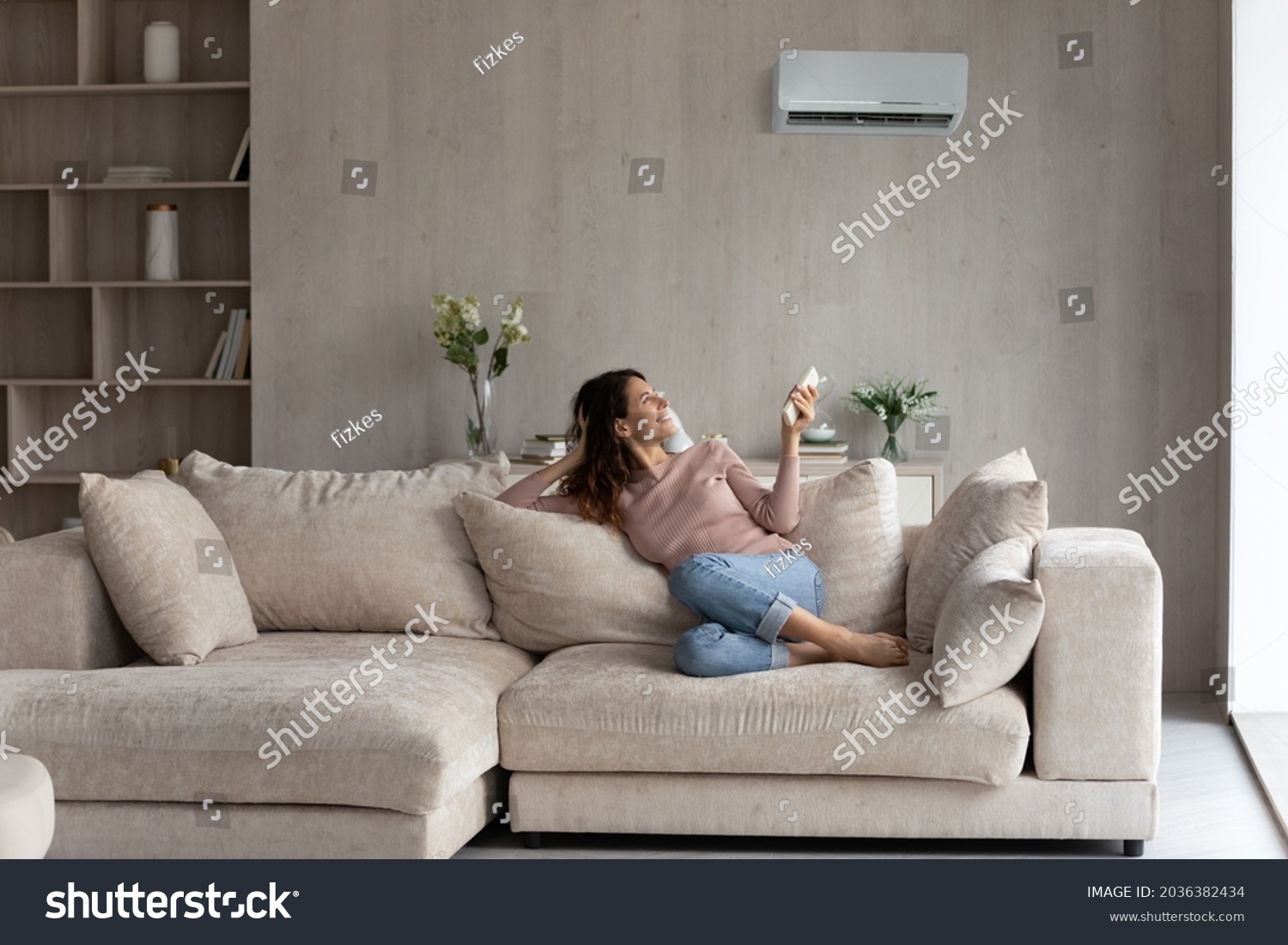 Relaxed young hispanic female homeowner sitting on huge comfortable couch, turning on air conditioner with remote controller, switching on cooler system, setting comfortable temperature in living room #2036382434