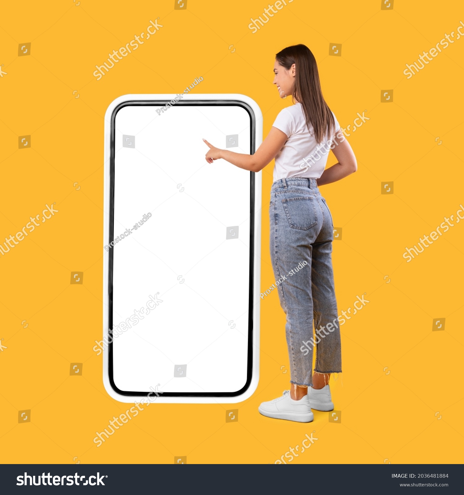 Full Body Length Back View Of Woman Using Big Smartphone With Blank White Screen And Touching Display Panel With Finger, Cheerful Lady Standing On Yellow Background, Ordering Food Delivery, Mock Up #2036481884