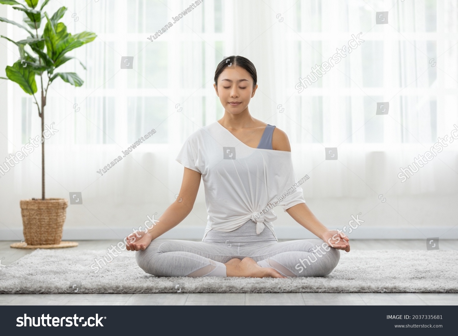 Calm of wellness Asian young woman sit on carpet breathing with yoga lotus pose,Yoga meditation of young healthy woman relax and comfortable at white cozy home,Yoga Exercise for Wellness Concept #2037335681