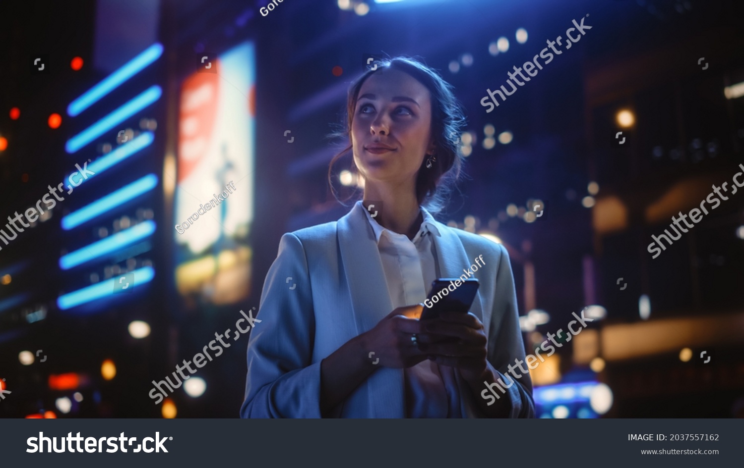 Beautiful Young Woman Using Smartphone Standing on the Night City Street Full of Neon Light. Portrait of Gorgeous Smiling Female Using Mobile Phone. #2037557162