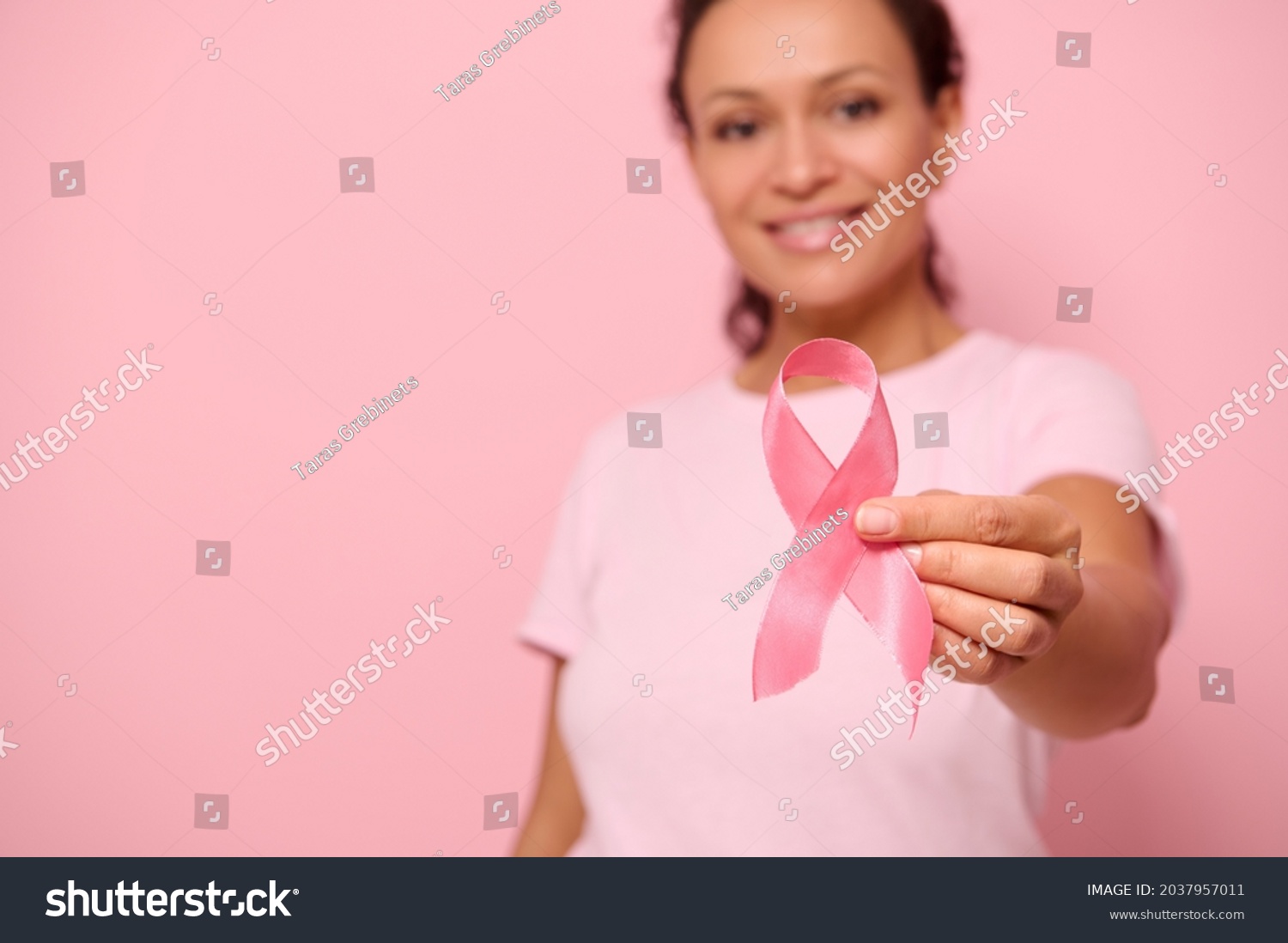 Blurred smiling mixed race woman in pink t-shirt hold satin ribbon in her hand. Breast and abdominal cancer awareness, October Pink day on colored background, copy space. Breast cancer support concept #2037957011