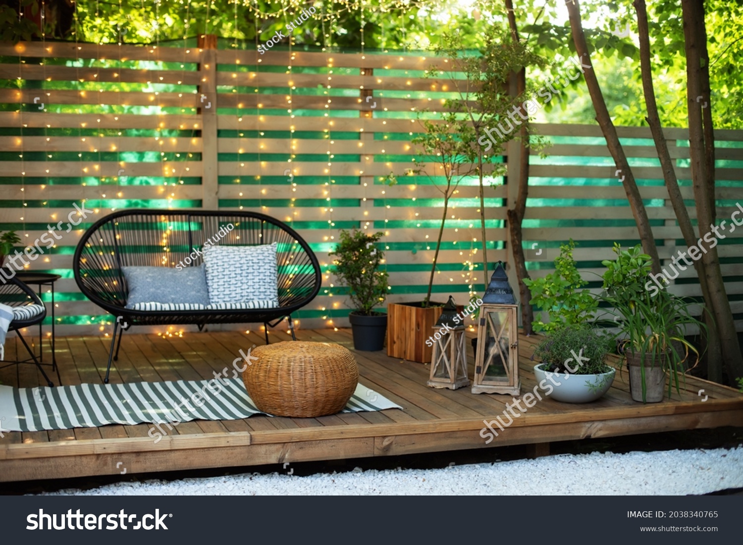 Modern lounge outdoors in backyard. Terrace house with plants, wooden wall and table, comfortable sofa, armchair and lanterns. Cozy space in patio or balcony. Wooden verande with garden furniture. 
 #2038340765