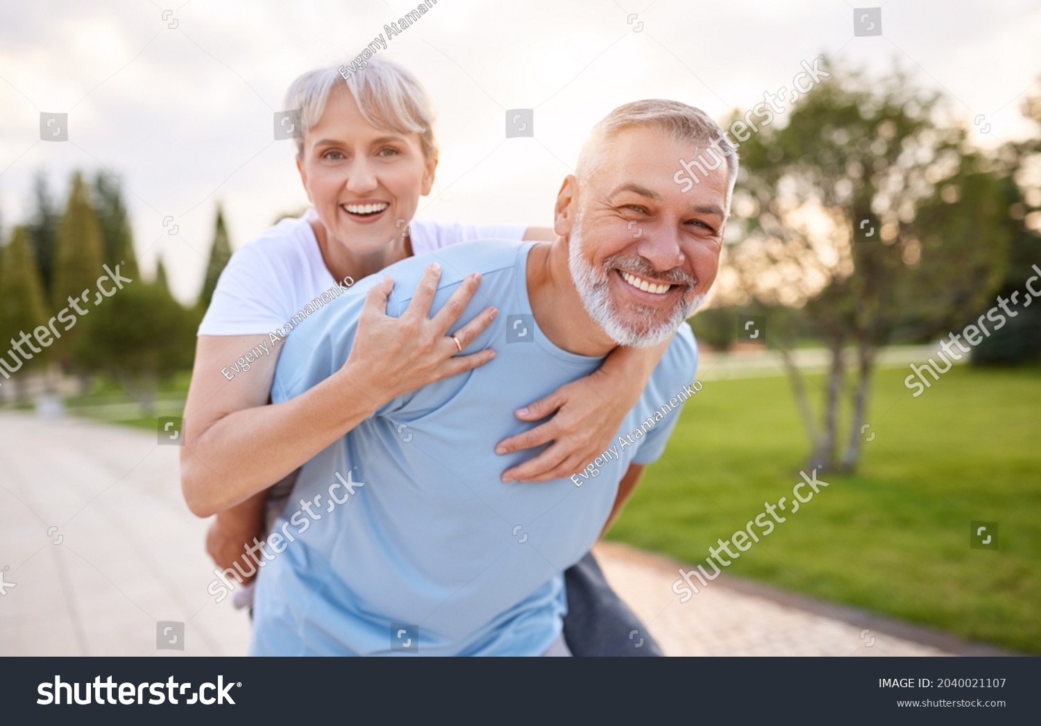 Portrait of lovely happy elderly couple on morning run outside in city park, retirees wife and husband rejoice in active lifestyle, smiling woman tenderly embracing her spouse after routine jogging #2040021107