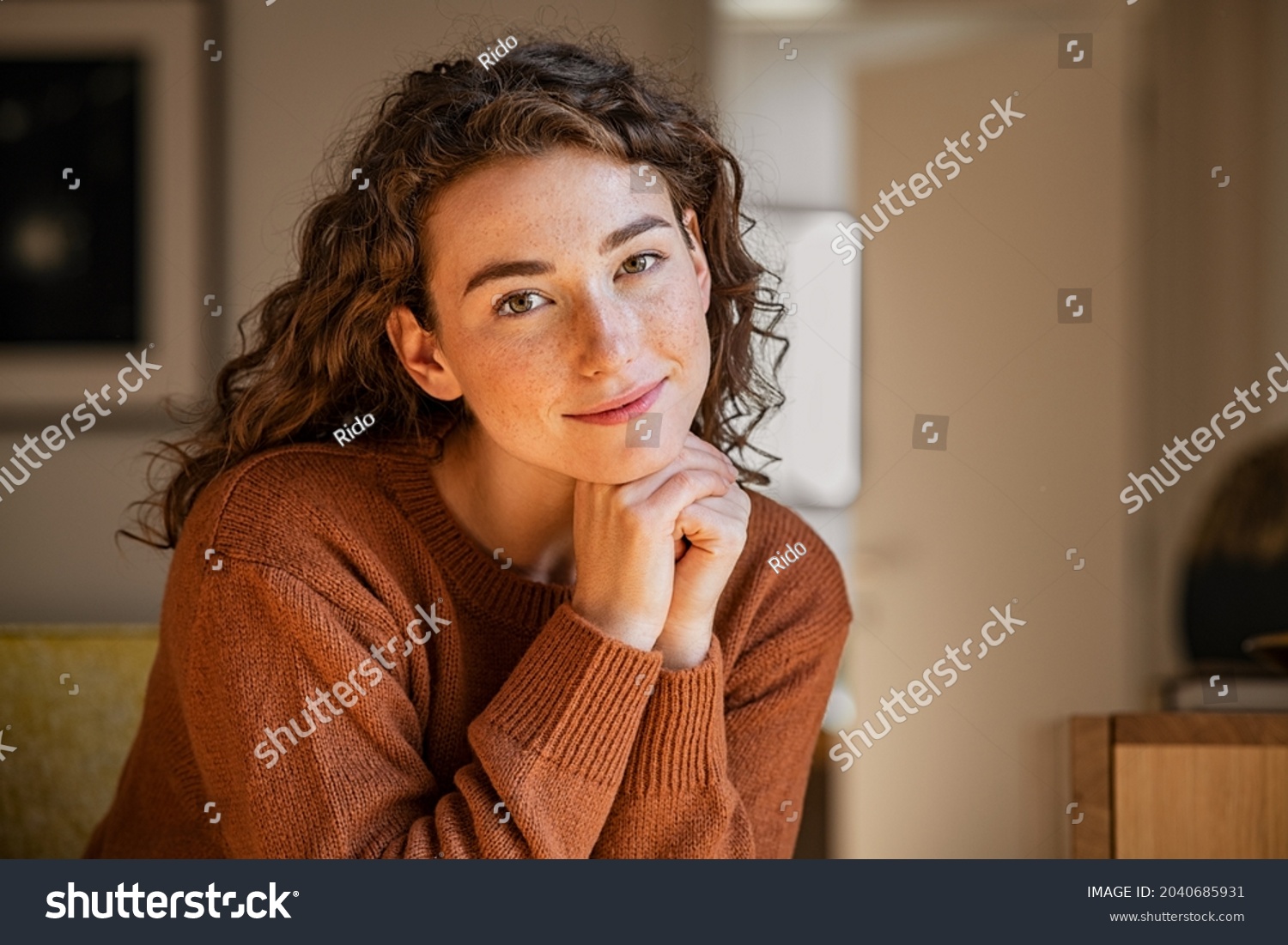 Portrait of satisfied young woman relaxing at home. Successful woman with hand on chin smiling and looking at camera. Beautiful natural girl stay at home with a serene expression. #2040685931