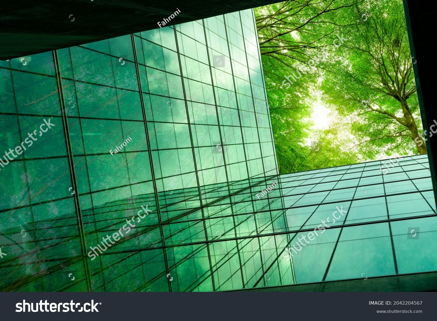 Eco-friendly building in the modern city. Green tree branches with leaves and sustainable glass building for reducing heat and carbon dioxide. Office building with green environment. Go green concept. #2042204567