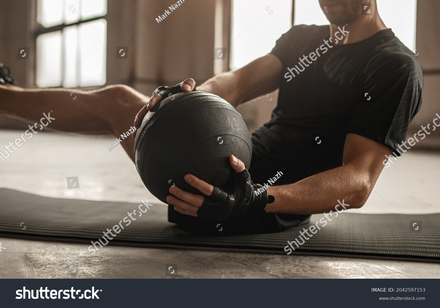 Side view of crop unrecognizable athletic male doing side twist exercise with medicine ball during intense functional training in gym #2042597153