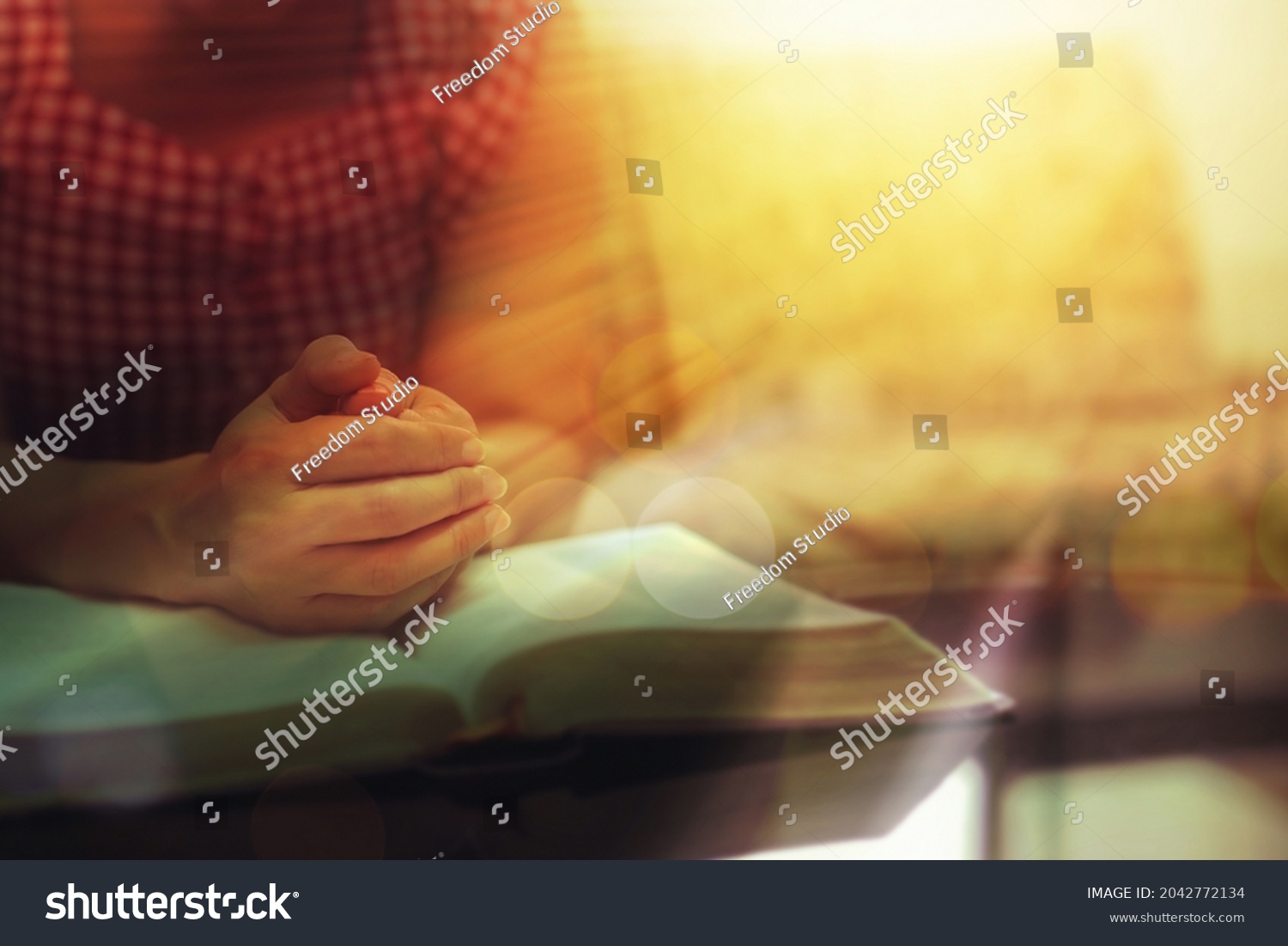 Close up of a woman hands praying on the open holy  bible on a table indoor with the windows light lay warm tone . Christian faith and trust concept  with copy space. Christian devotional background. #2042772134