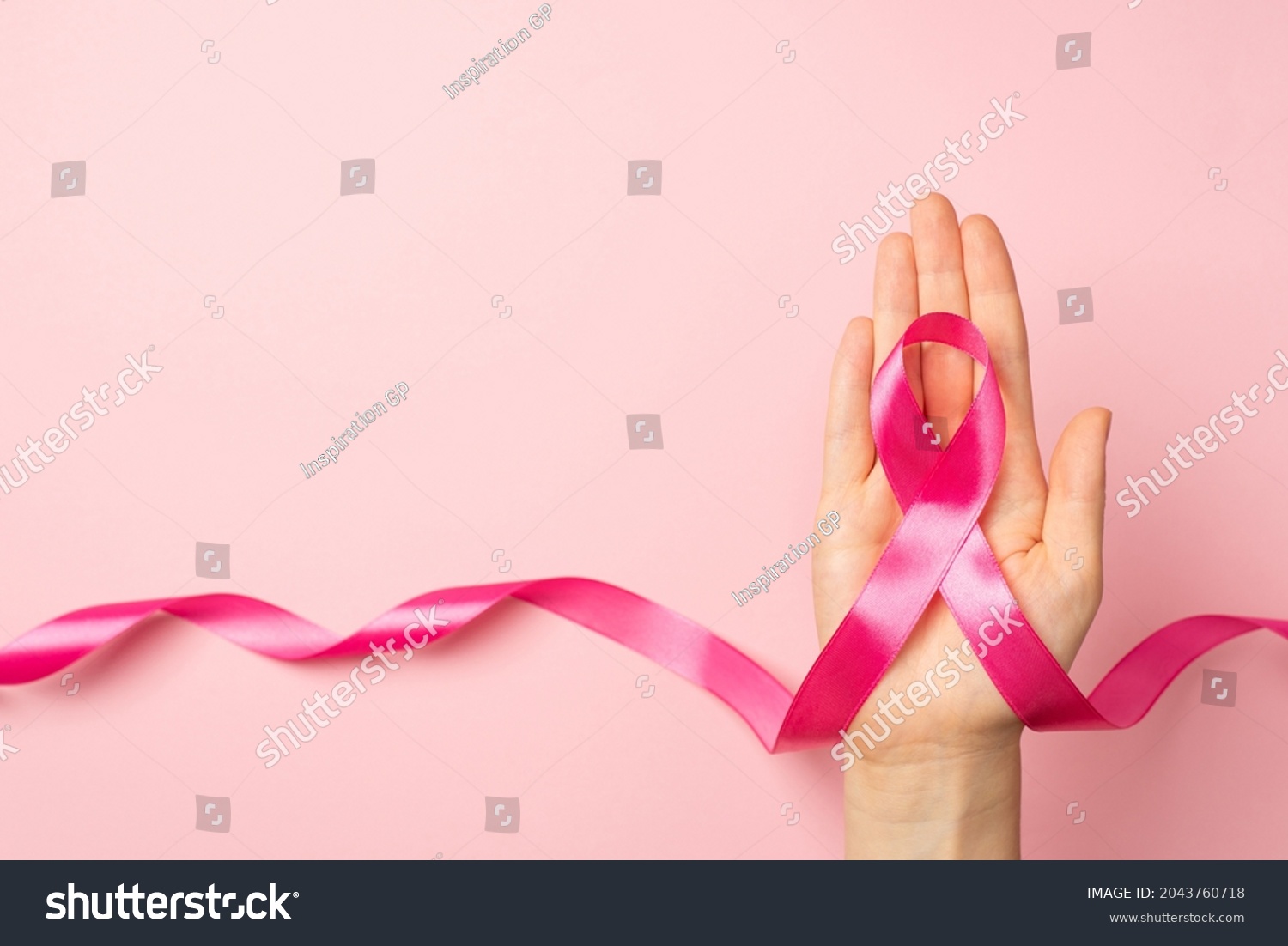 First person top view photo of female hand holding pink ribbon in palm symbol of breast cancer awareness on isolated pastel pink background with copyspace #2043760718