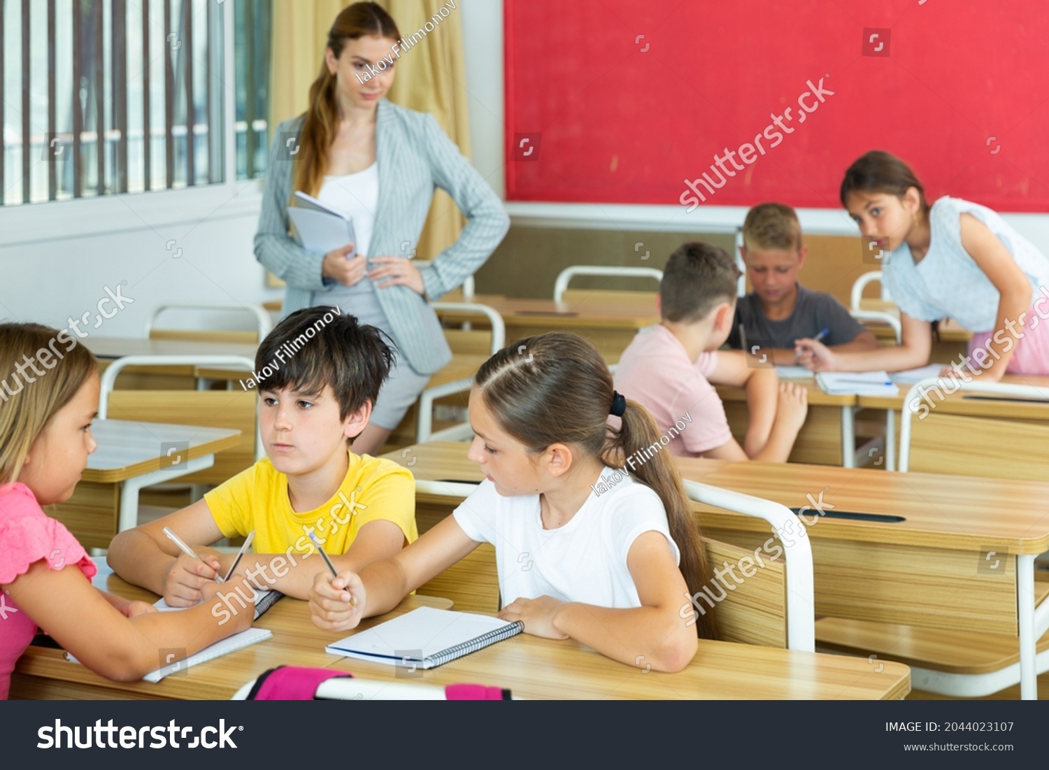 Schoolchildren performing group tasks in classroom. Teacher standing beside and observing. #2044023107