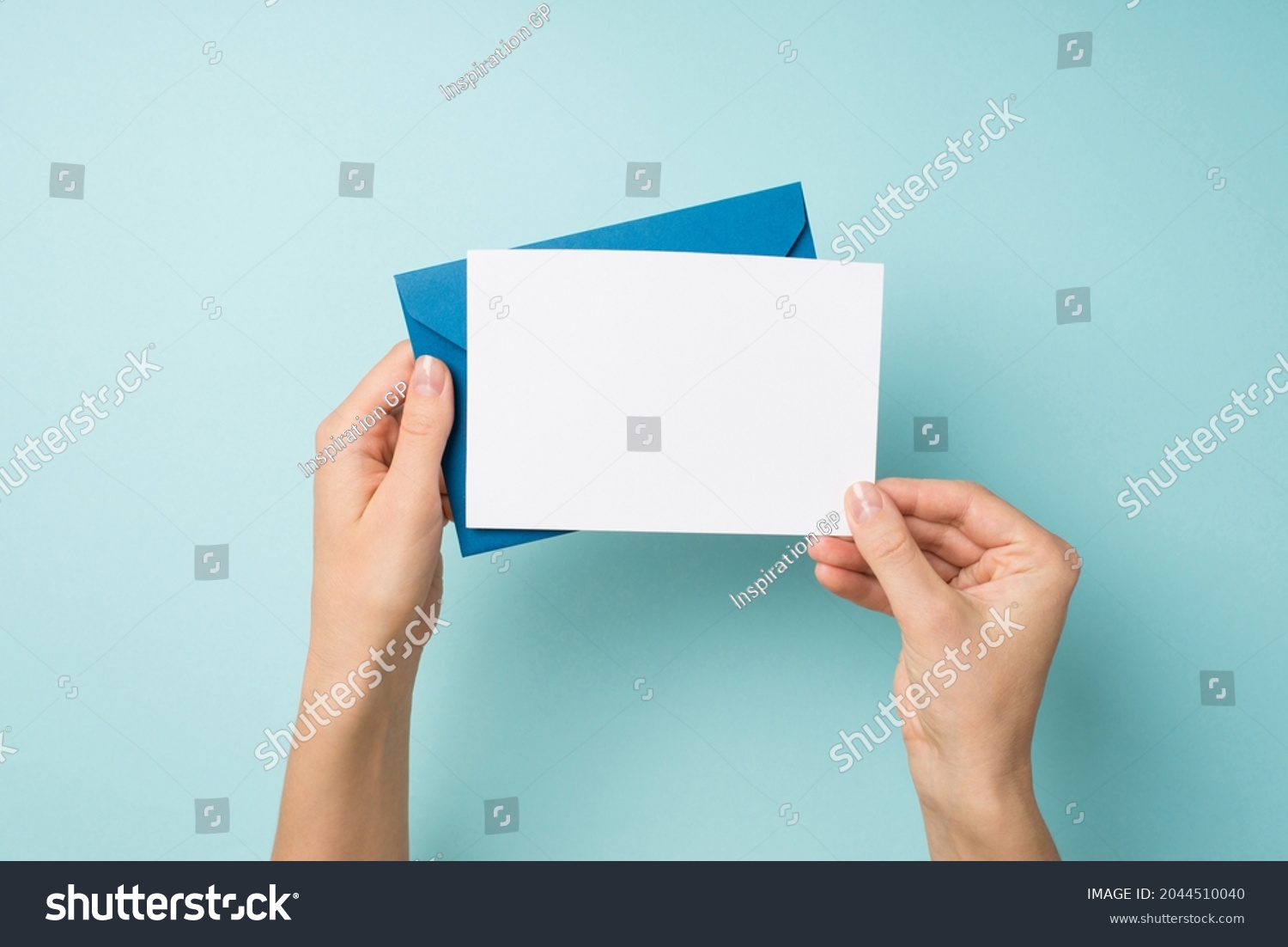 First person top view photo of hands holding blue envelope and white card on isolated pastel blue background with empty space #2044510040