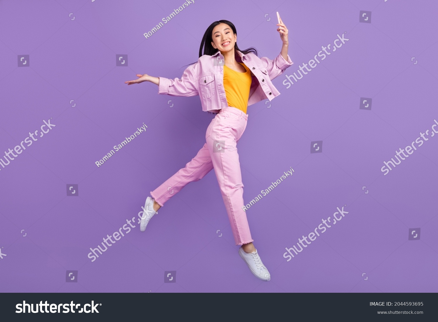 Full size profile photo of funky young brunette lady jump hold telephone wear jacket jeans sneakers isolated on violet background #2044593695