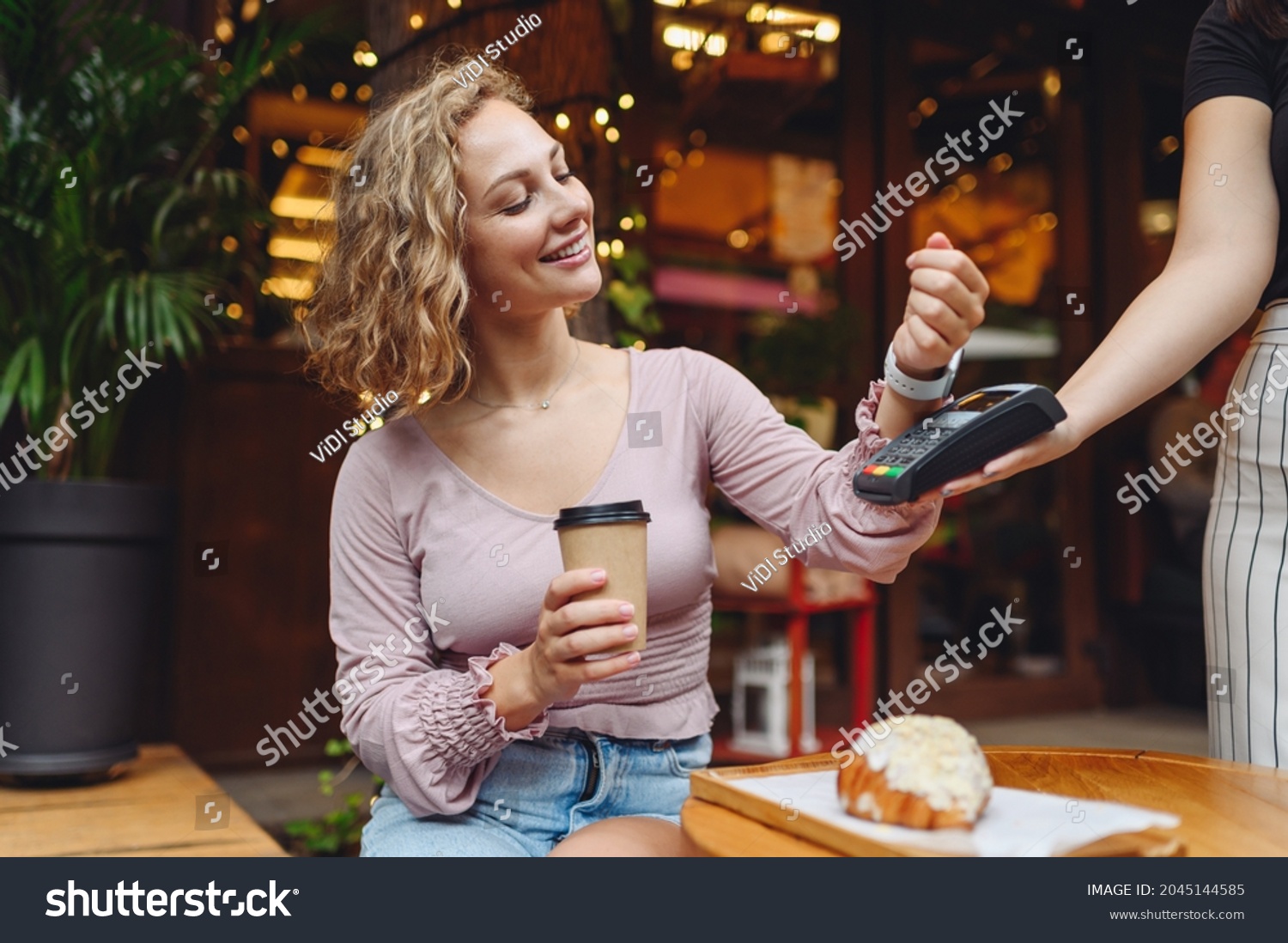 Young woman in casual clothes at cafe buy breakfast sit at table hold wireless bank payment terminal smart watch to process acquire payments drink coffee relax in restaurant during free time indoors. #2045144585