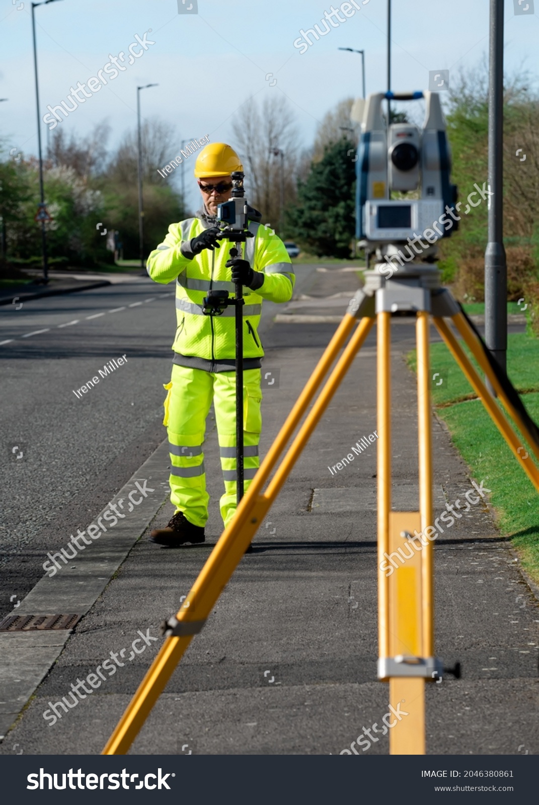 Land surveyor performing initial survey of the road levels and kerb lines before start of construction works using robotic tacheometer controlled by remote control and prism on pogo. #2046380861