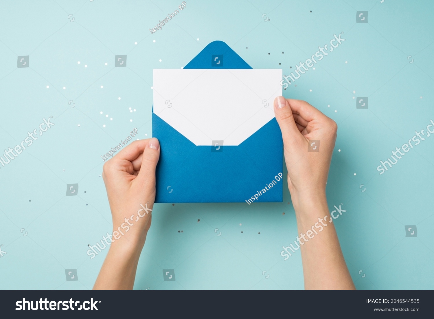 First person top view photo of hands holding open blue envelope with white card over sequins on isolated pastel blue background with empty space #2046544535