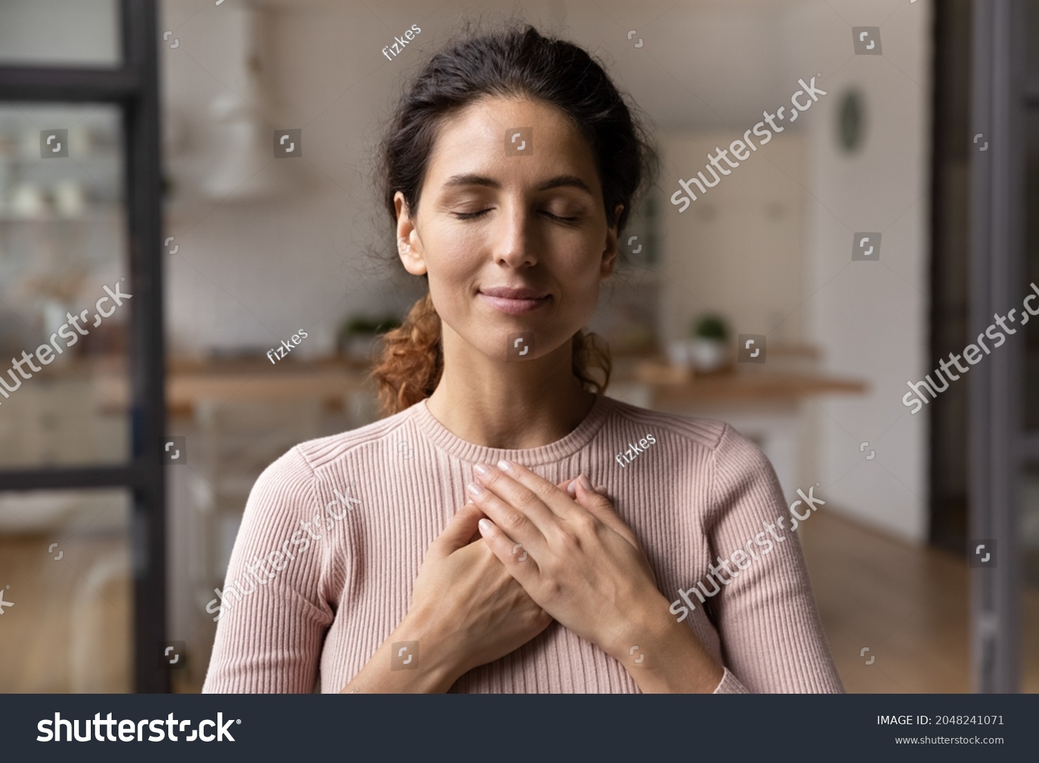 Close up of calm young Caucasian woman hold hands on heart chest feel grateful and thankful. Happy millennial female show gratitude, love and care, pray or visualize. Religion, faith concept. #2048241071