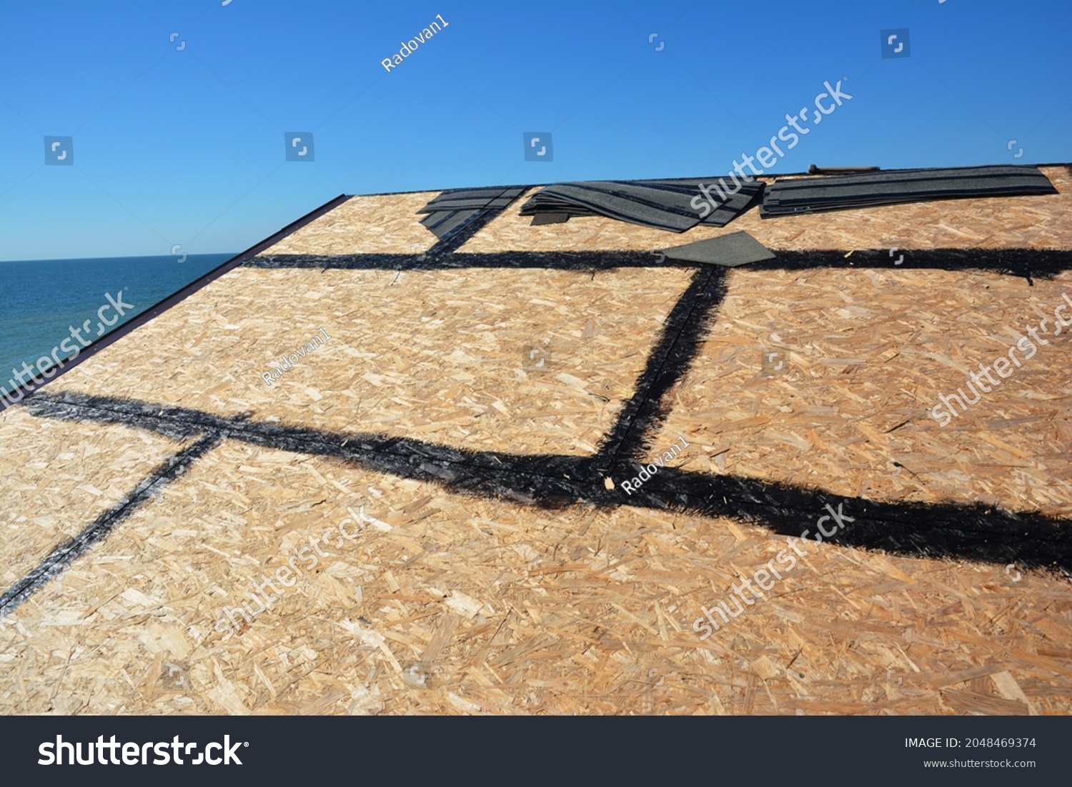 Roofing construction and waterproofing. A close-up of OSB roof deck, roof sheathing with hot rubberized asphalt, bitumen, tar waterproofing before asphalt shingles installation. #2048469374