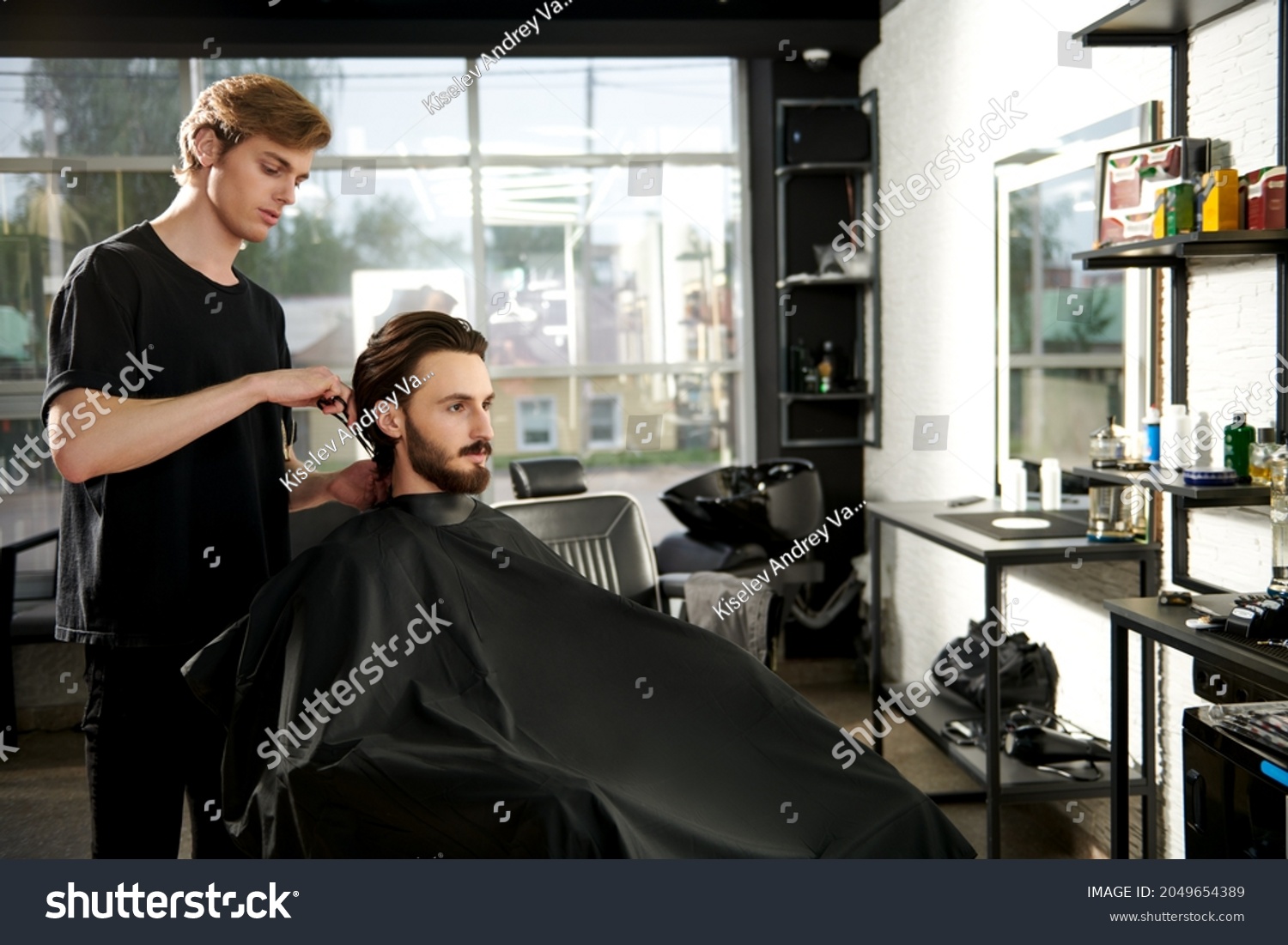 Hairstylist serving a client at a barbershop. Handsome brunet man visiting a hairstylist. Modern hairdressing saloon.  #2049654389
