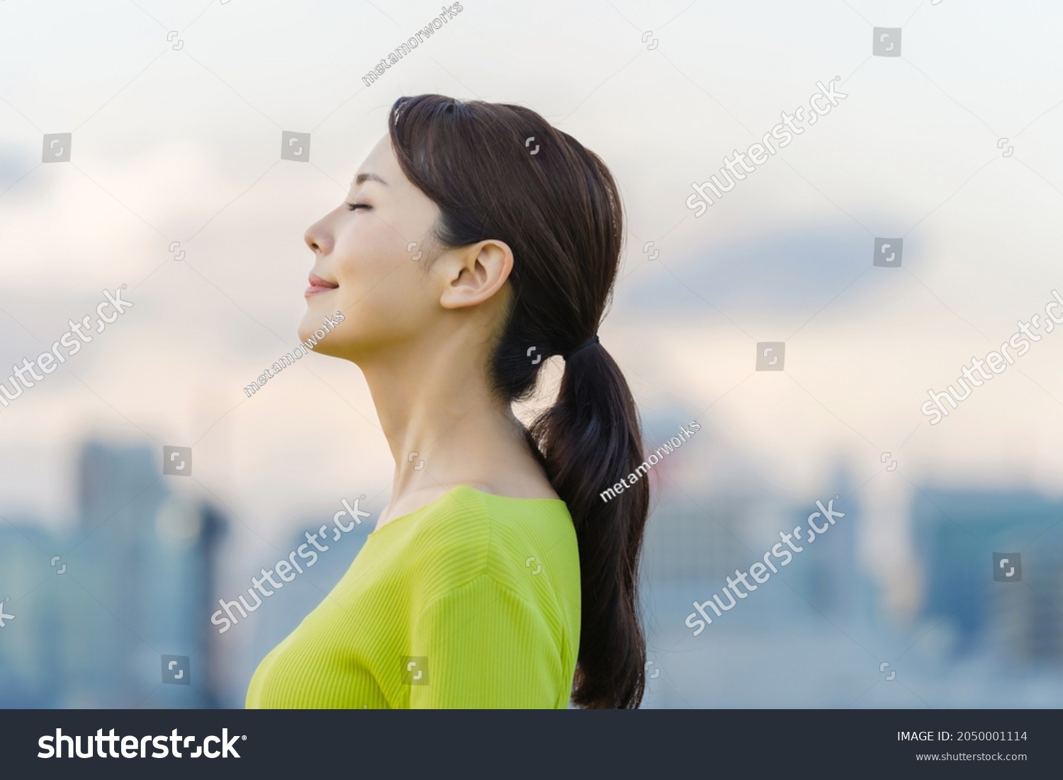 Young asian woman closing eyes in front of the city. #2050001114