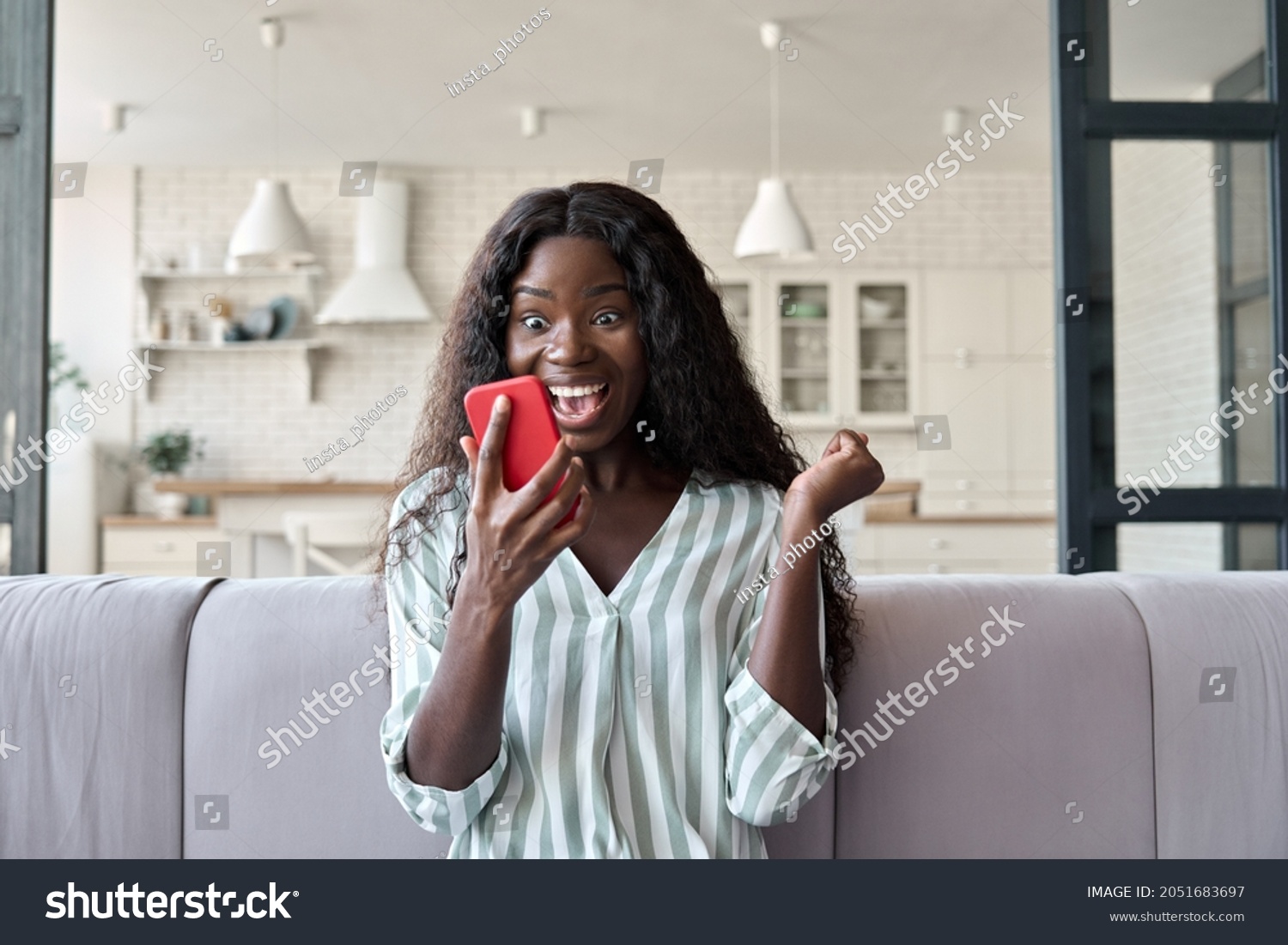 Young African girl at home reading message on mobile phone on unexpected news, happy client winning online shopping promo, gets prize in social media giveaway. Good luck big win concept. #2051683697