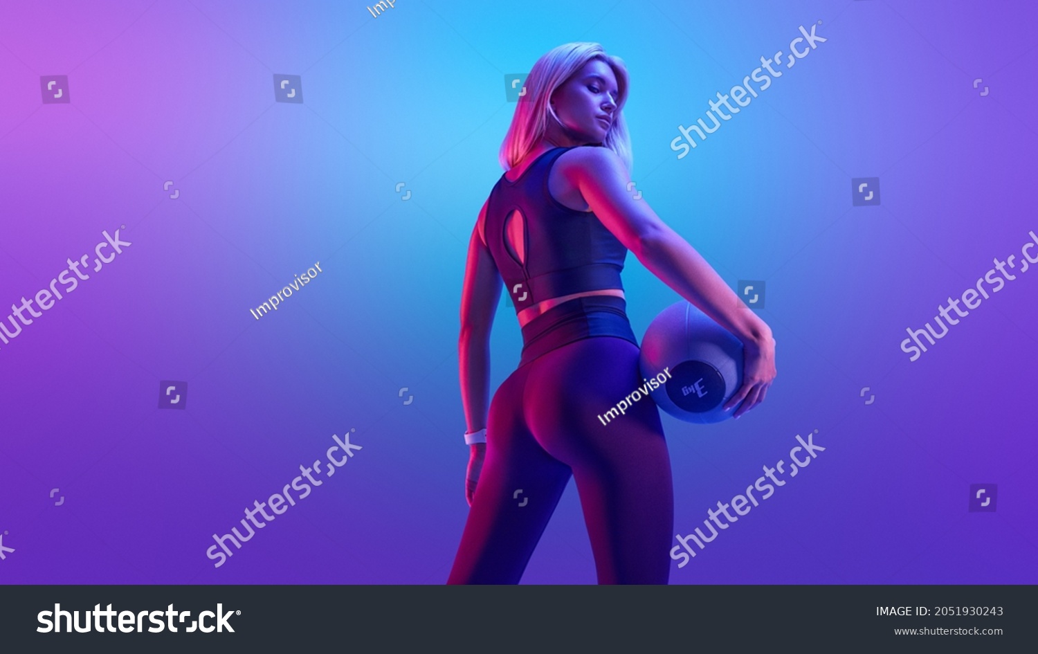 Confident fitness woman posing with a medicine ball. Attractive blonde sportswoman portrait holding with medicine fitness ball neon style creative light. #2051930243