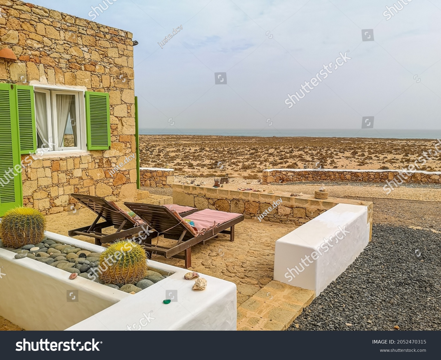 Sunbeds in terrace of an old stone house with majestic desert view. Boa Vista Island, Cape Verde, Africa. Selective focus on the building exterior, blurred background. #2052470315