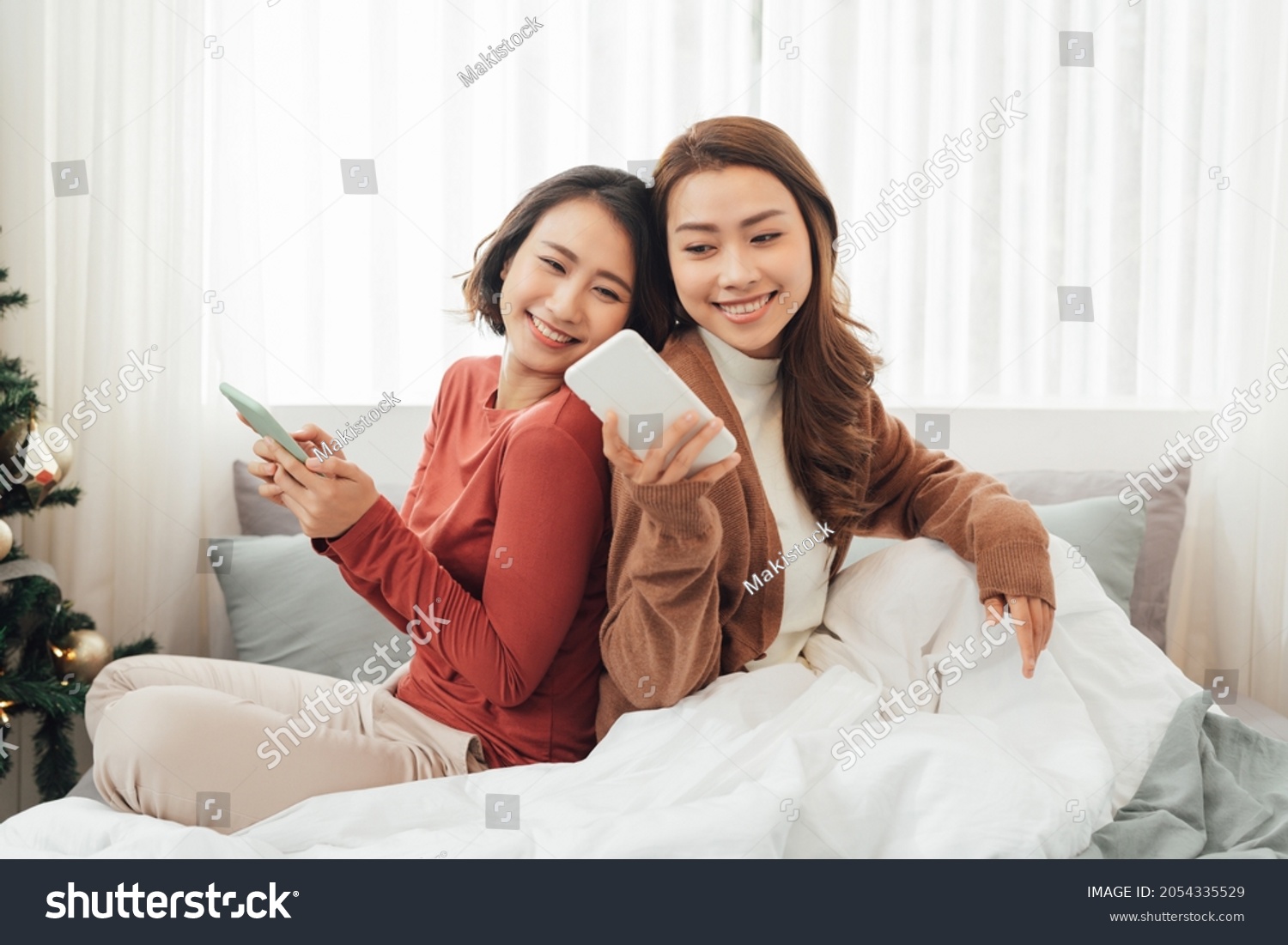 Smiling Two Asian young lovely couple repose on white bed and happy playing with smartphone and social media. #2054335529