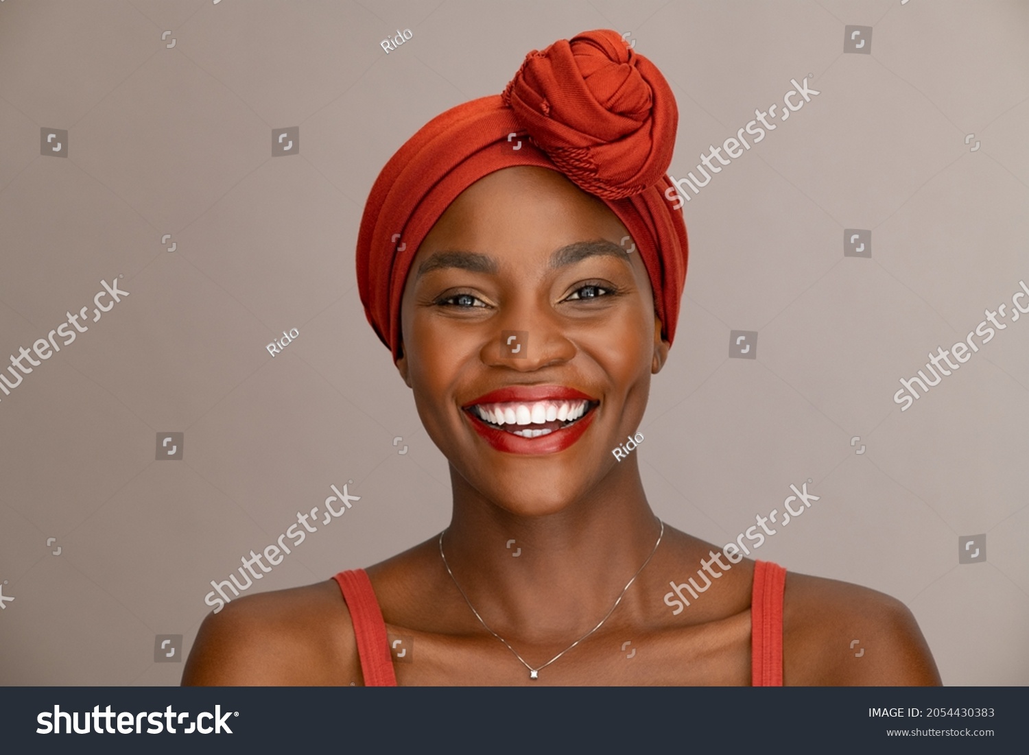 Portrait of beautiful african woman with red headscarf against brown background with copy space. Cheerful black mid woman wearing ethnicity headband. Mature happy lady with traditional clothes. #2054430383
