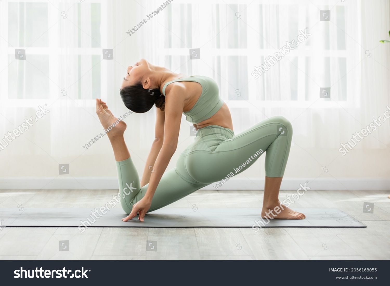 Side view of Asian woman wearing green sportwear doing Yoga exercise,Yoga One Legged King Pigeon pose or Eka Pada Rajakapotasana,Calm of healthy young woman breathing and meditation with yoga at home #2056168055