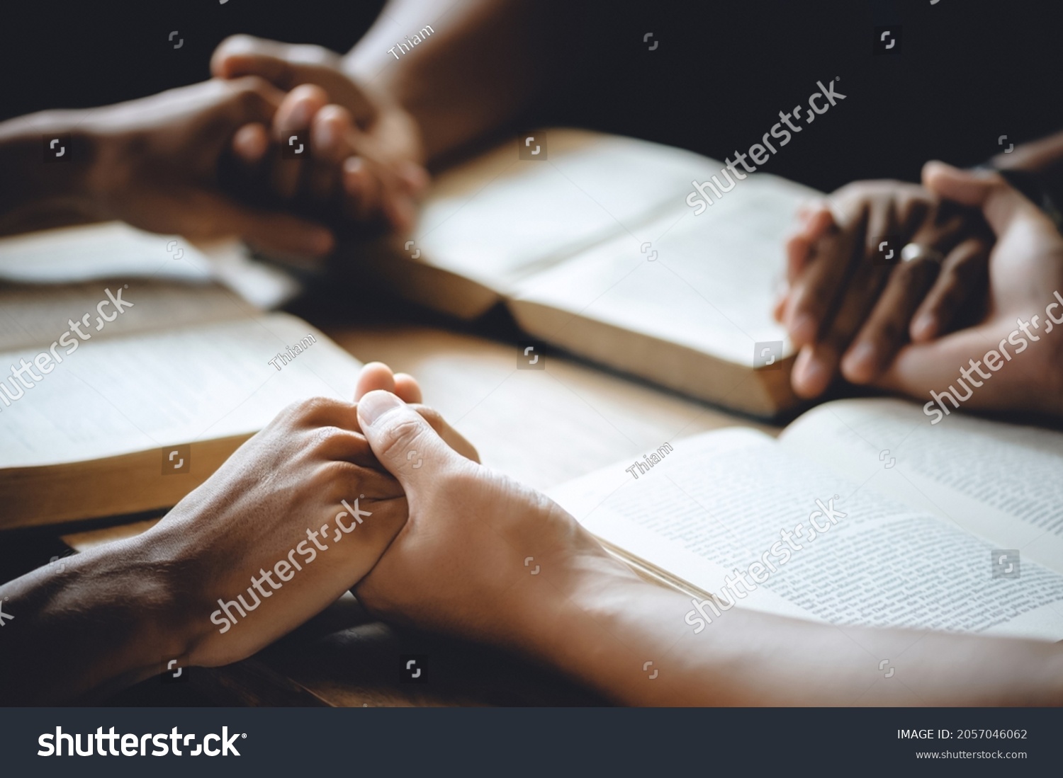 Christian group of people holding hands praying worship to believe and Bible on a wooden table for devotional or prayer meeting concept. #2057046062