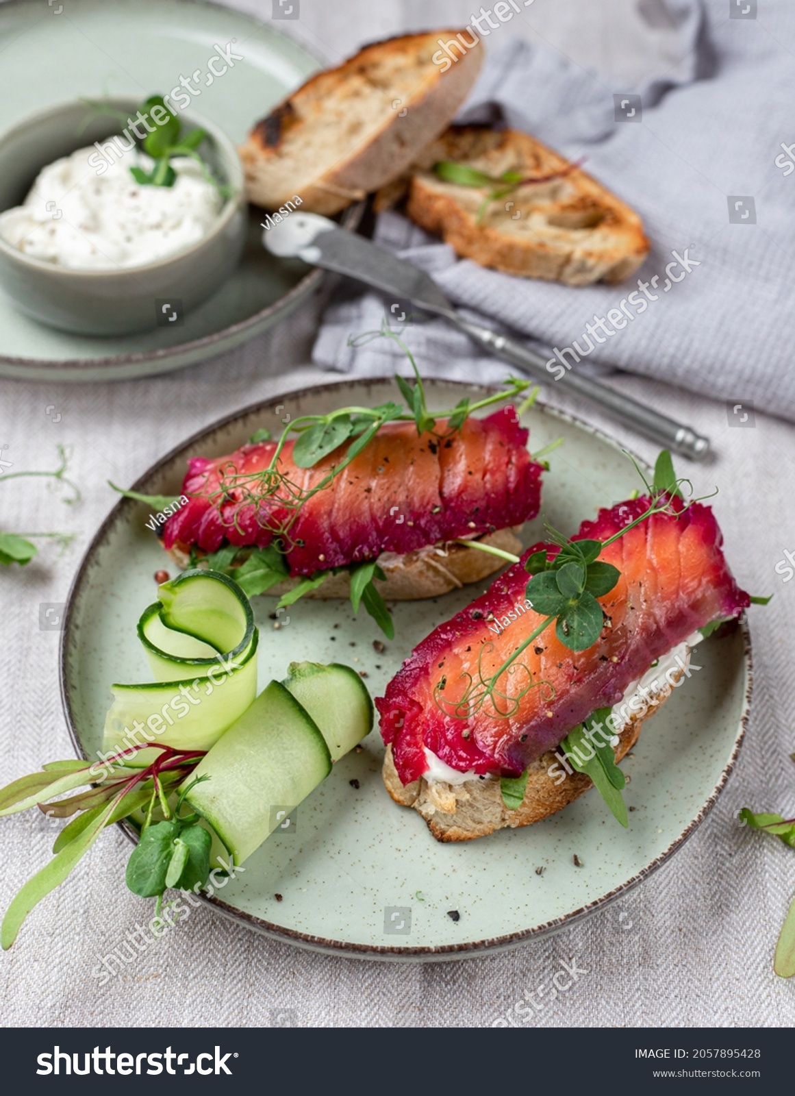 Healthy sandwiches with sourdough crisp bread slices, sour cream, beetroot cured salmon and cucumber on green ceramic plate, top view

A #2057895428